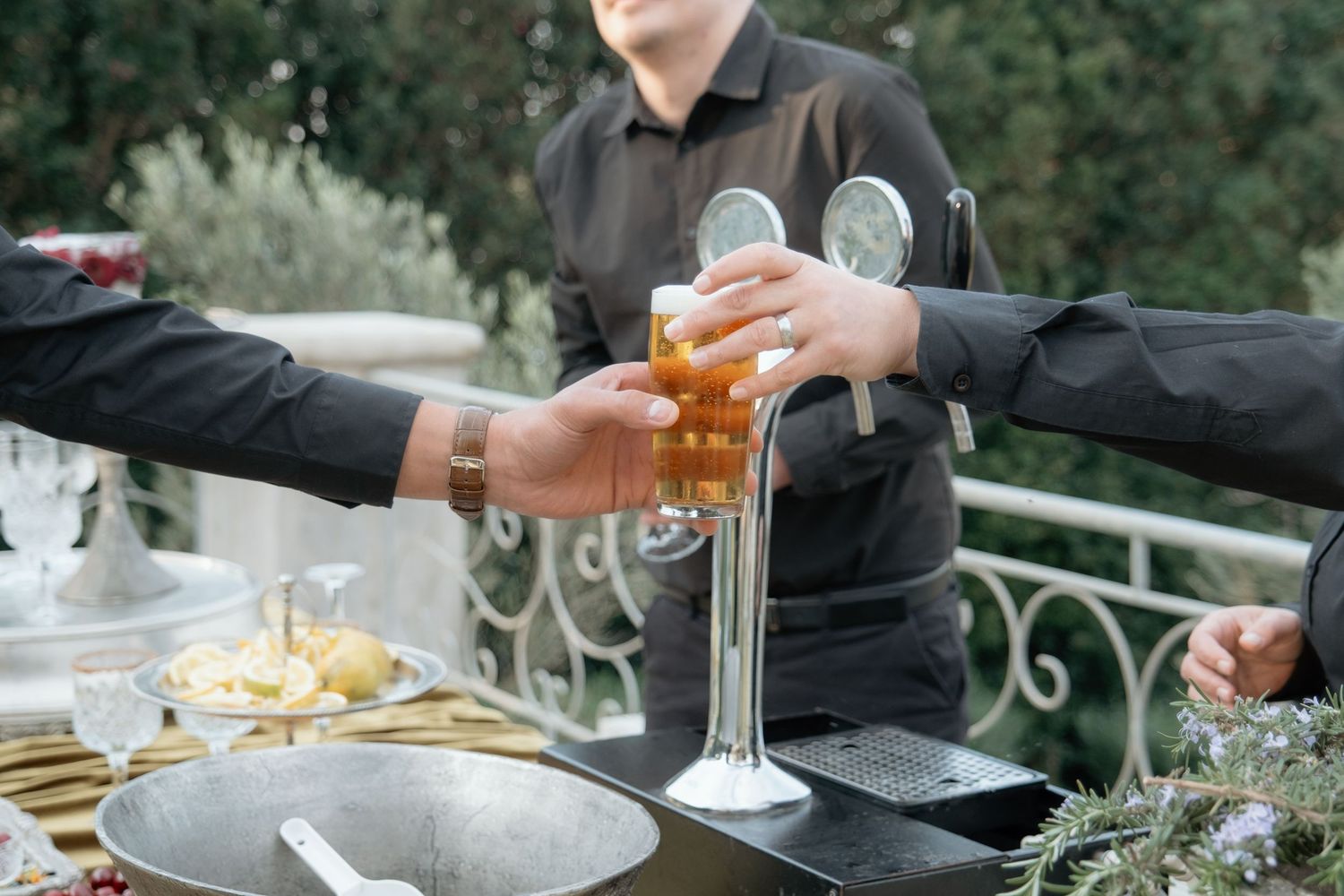 Bartender serving beer at outdoor wedding reception bar with guests reaching for drinks.