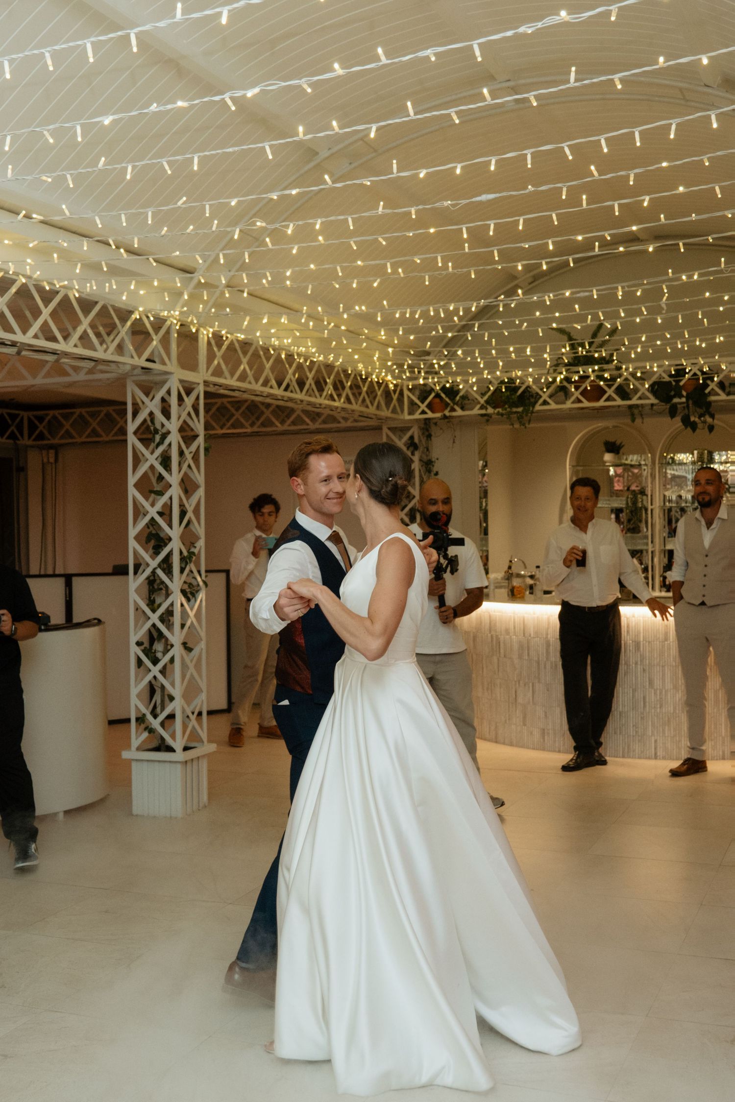 Bride and groom share their first dance under fairy lights at elegant wedding reception venue.