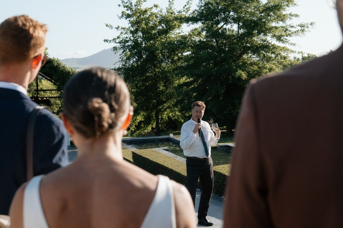 Officiant speaking outdoors to bride and groom with mountain landscape in the background.