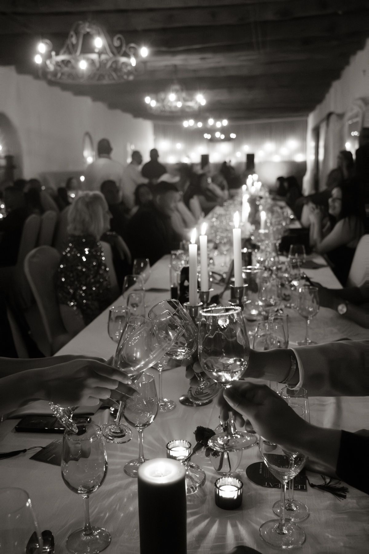 Black and white photo of candlelit wedding reception dinner with guests seated along long decorated banquet table.
