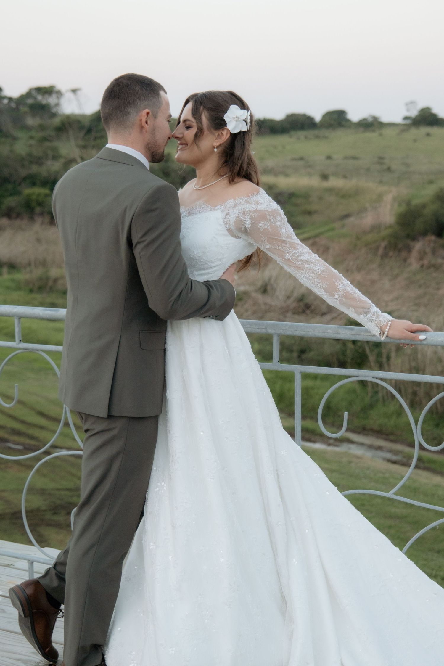 Bride and groom sharing romantic moment on white railing balcony with green landscape.