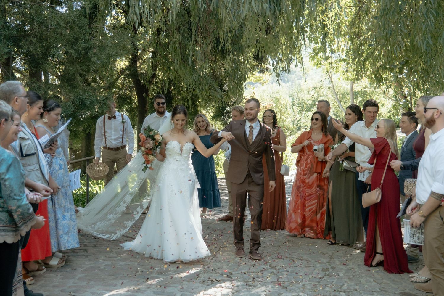 Bride and groom walk back down the aisle after ceremony through cheering guests in a garden.