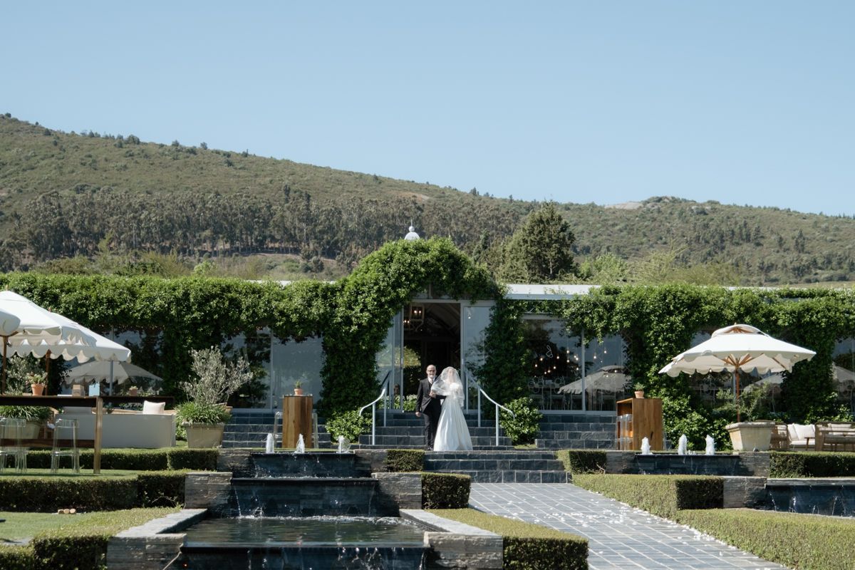 Bride and groom share a moment in ivy-covered venue surrounded by manicured hedges and hills.