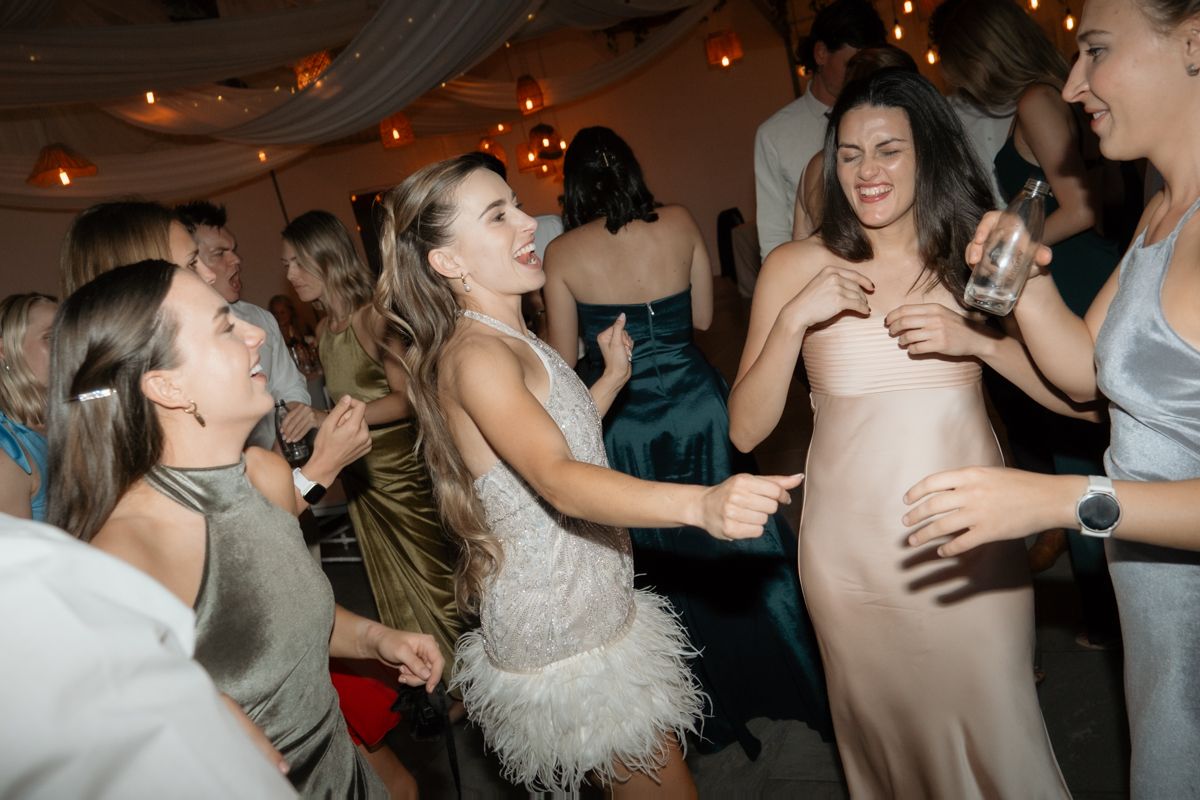 Bride in feathered white dress dances joyfully with guests at lively wedding reception celebration.