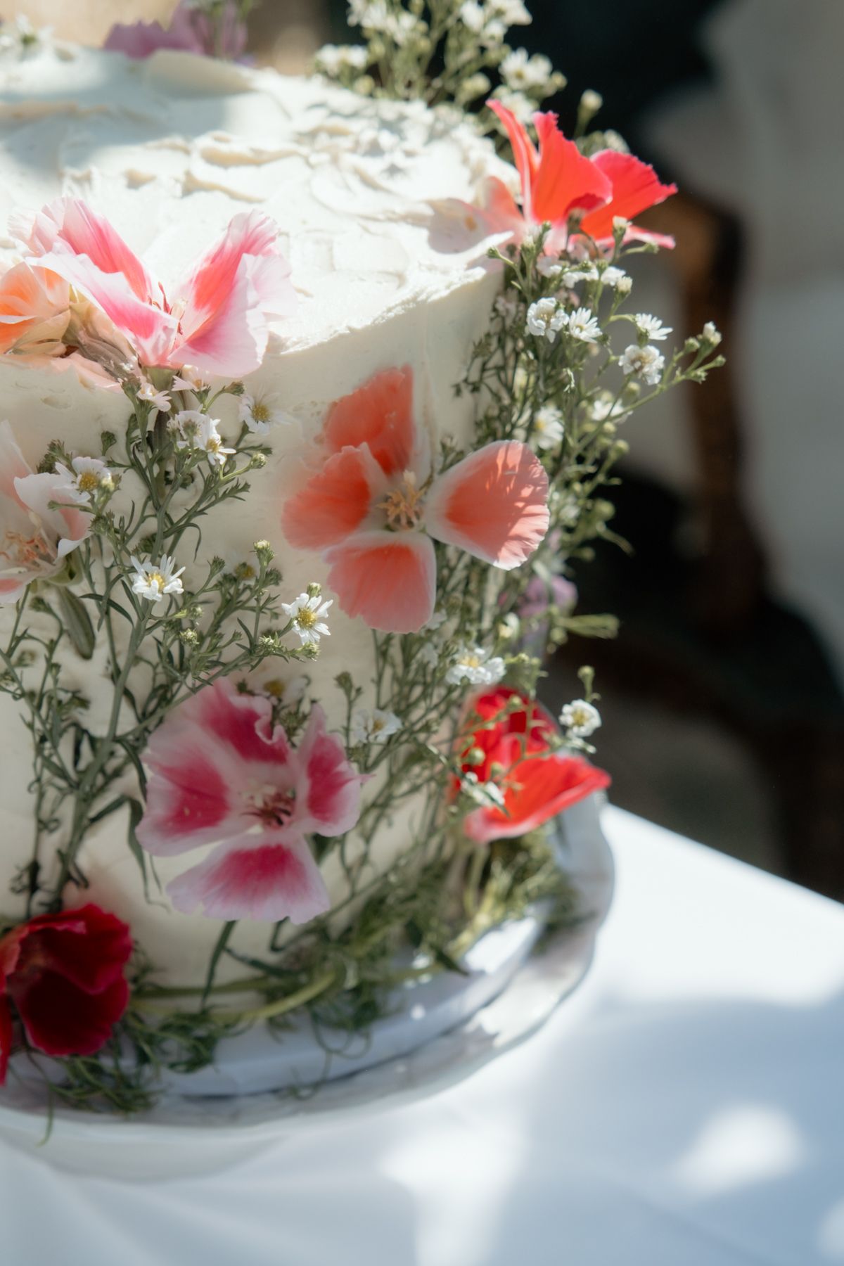 Two-tier white wedding cake decorated with fresh pink and red flowers and greenery.