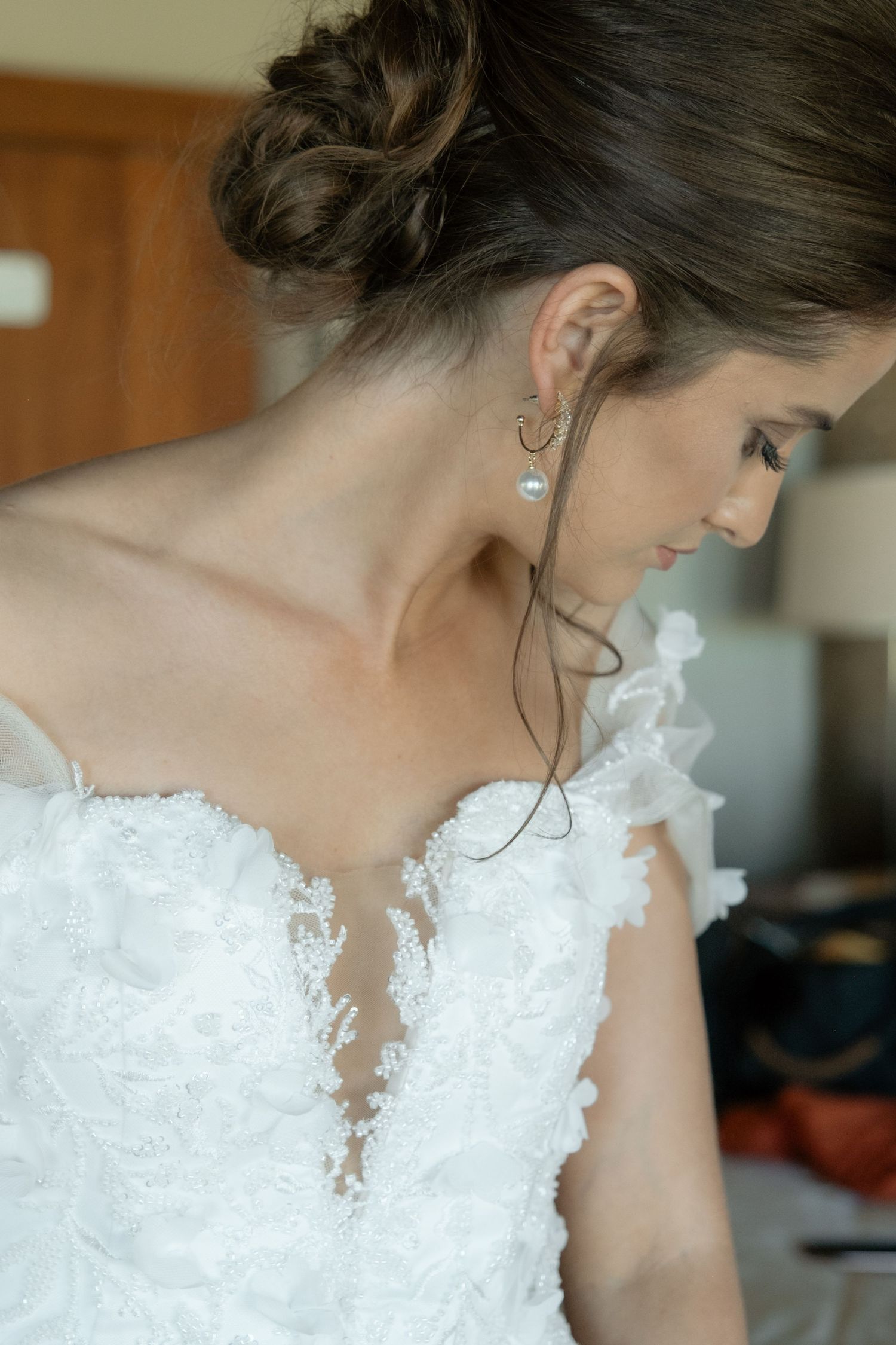 Close-up of bride wearing pearl earrings in a lace off-shoulder wedding dress with updo hairstyle.