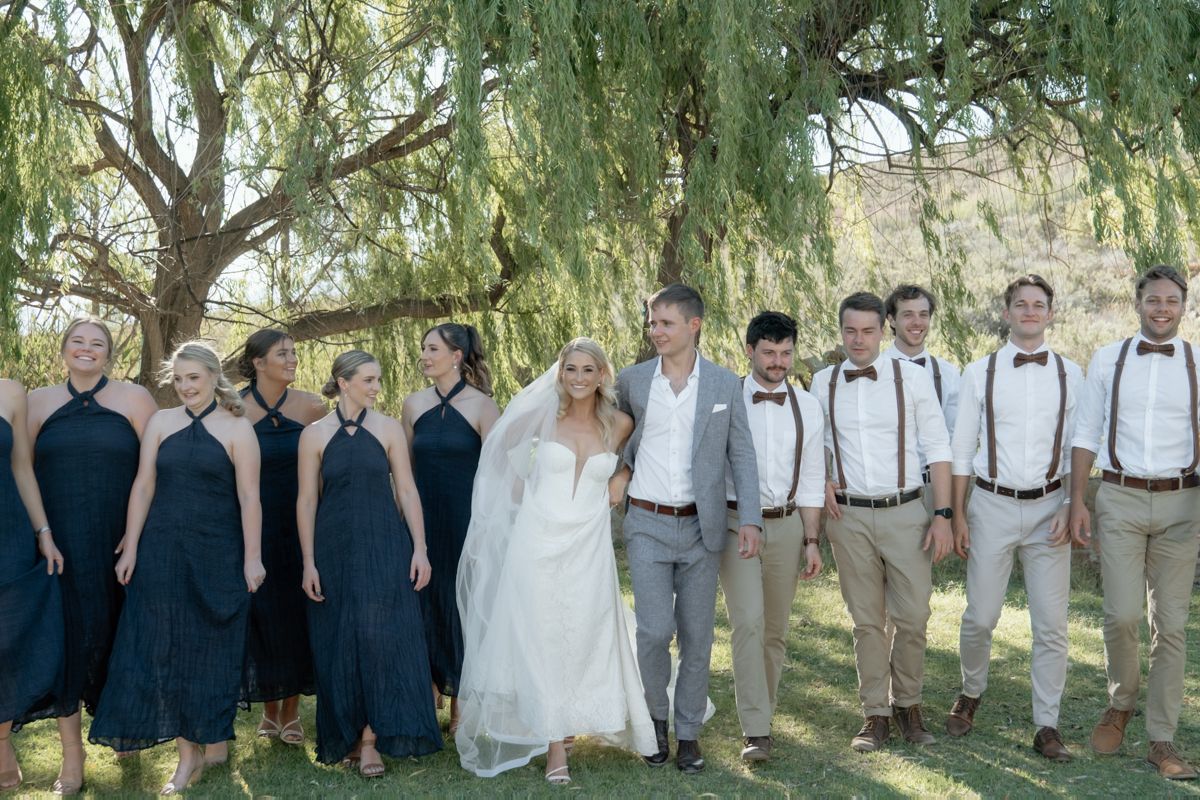 Wedding party walking together, bridesmaids in navy dresses, groomsmen in suspenders.