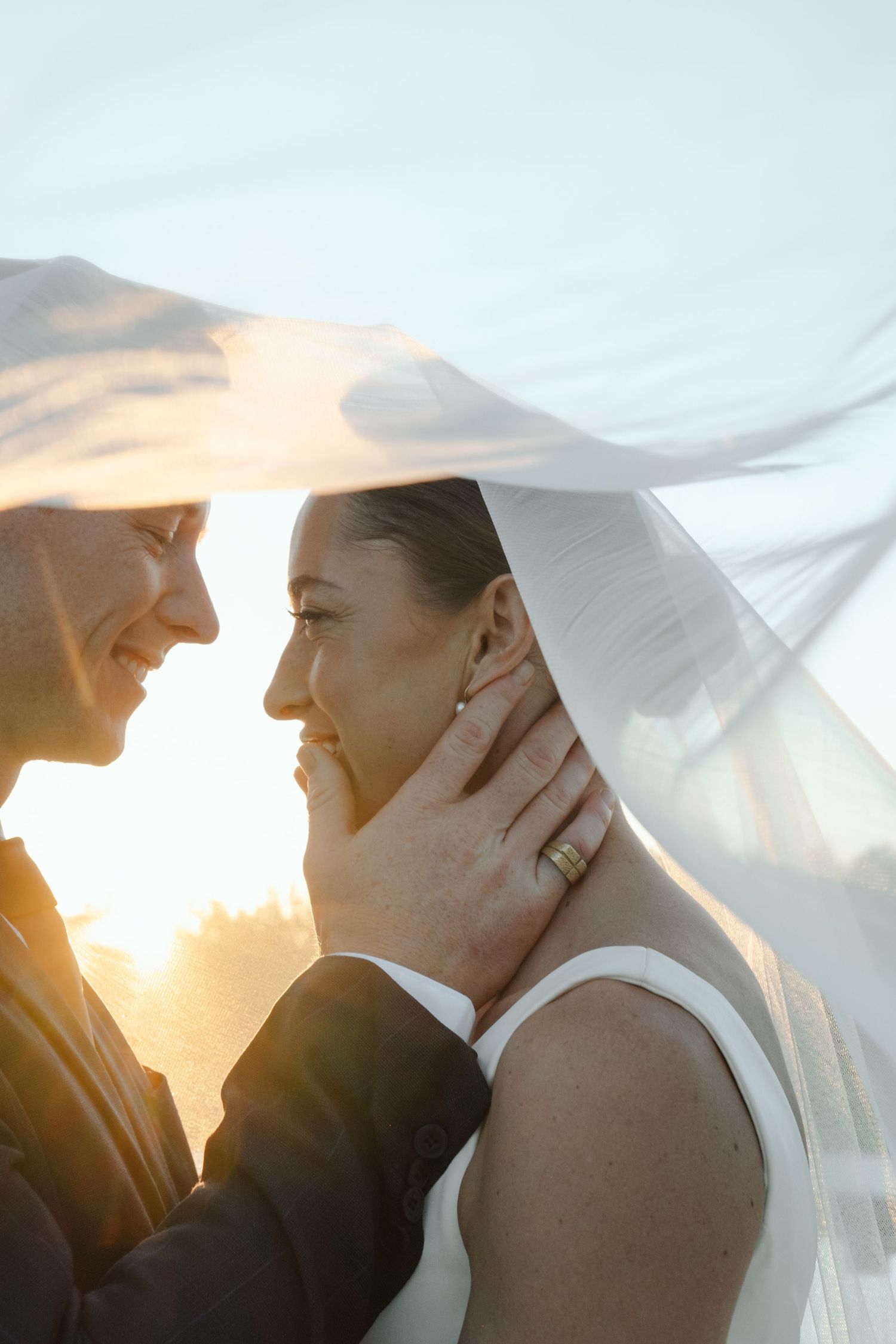 Bride and groom sharing a romantic moment under a veil at golden hour sunset.