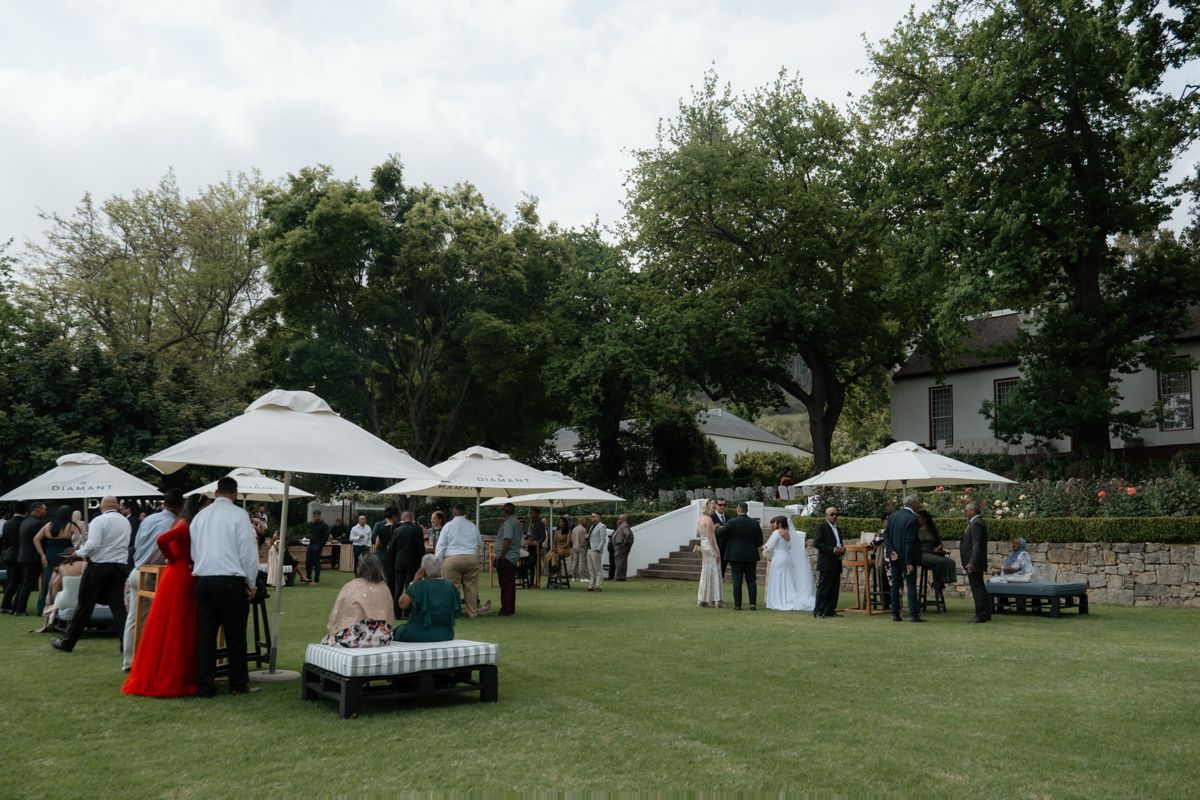 Wide shot of wedding guests mingling on a lawn with white umbrellas at an estate venue.