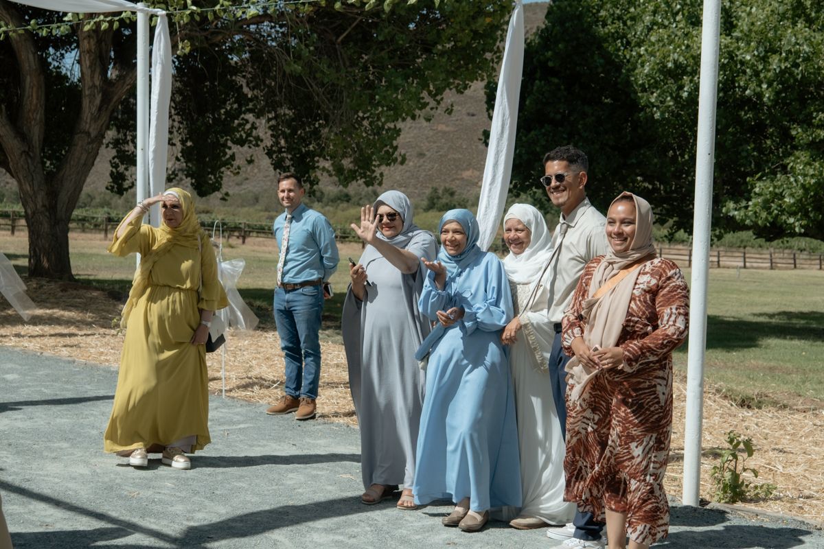 Group of wedding guests in colorful traditional attire posing together at outdoor ceremony.