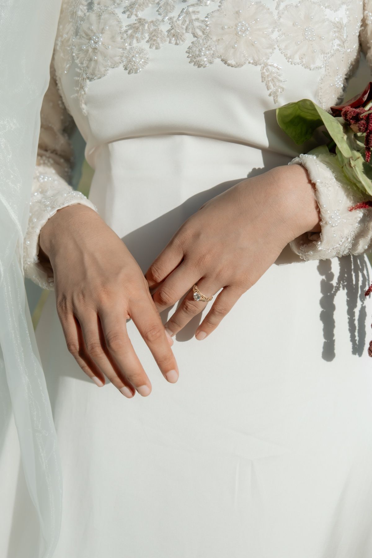 Close-up of bride's hands showing diamond engagement ring with white wedding dress and bouquet.