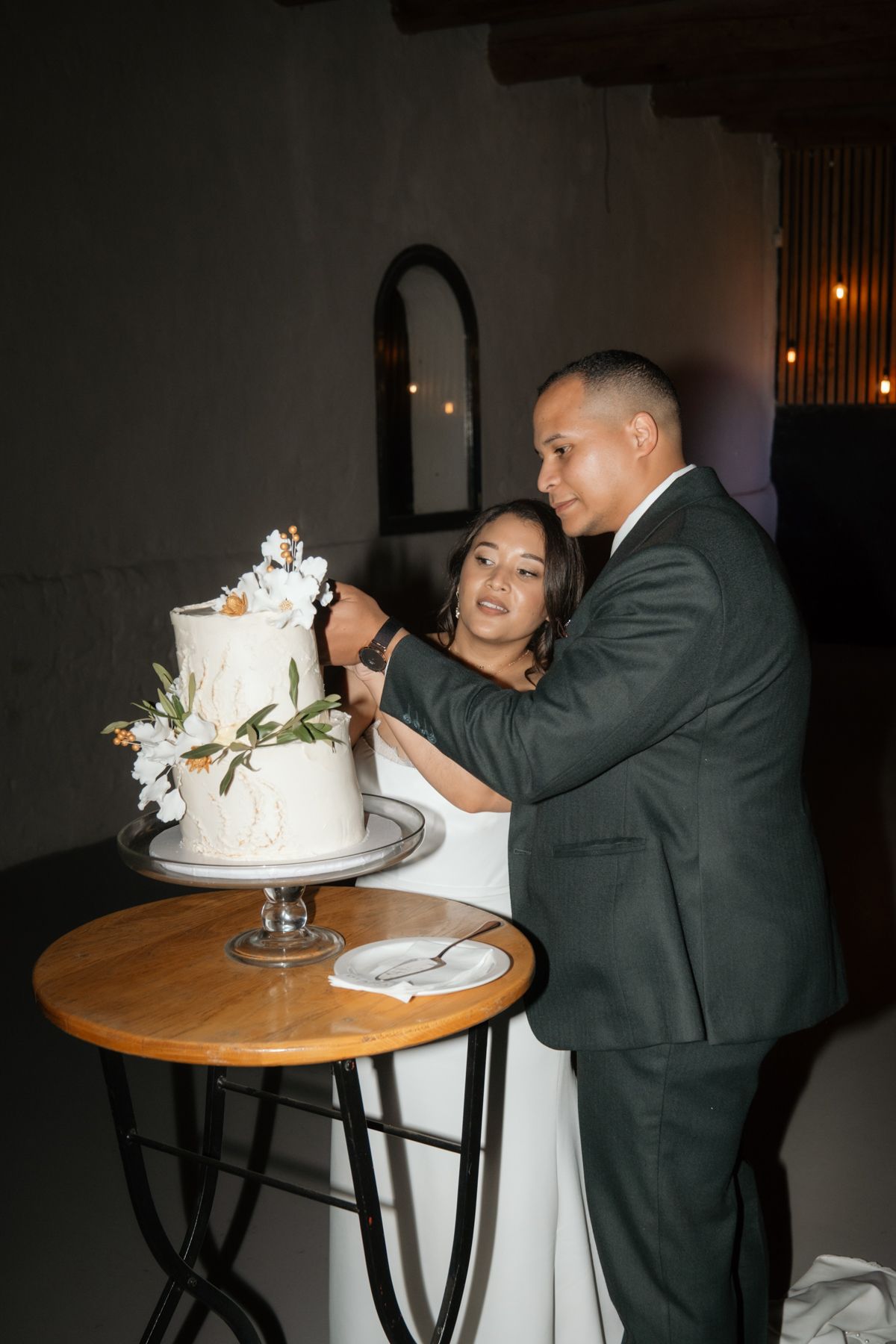 Bride and groom cutting their white floral wedding cake together at their wedding reception.