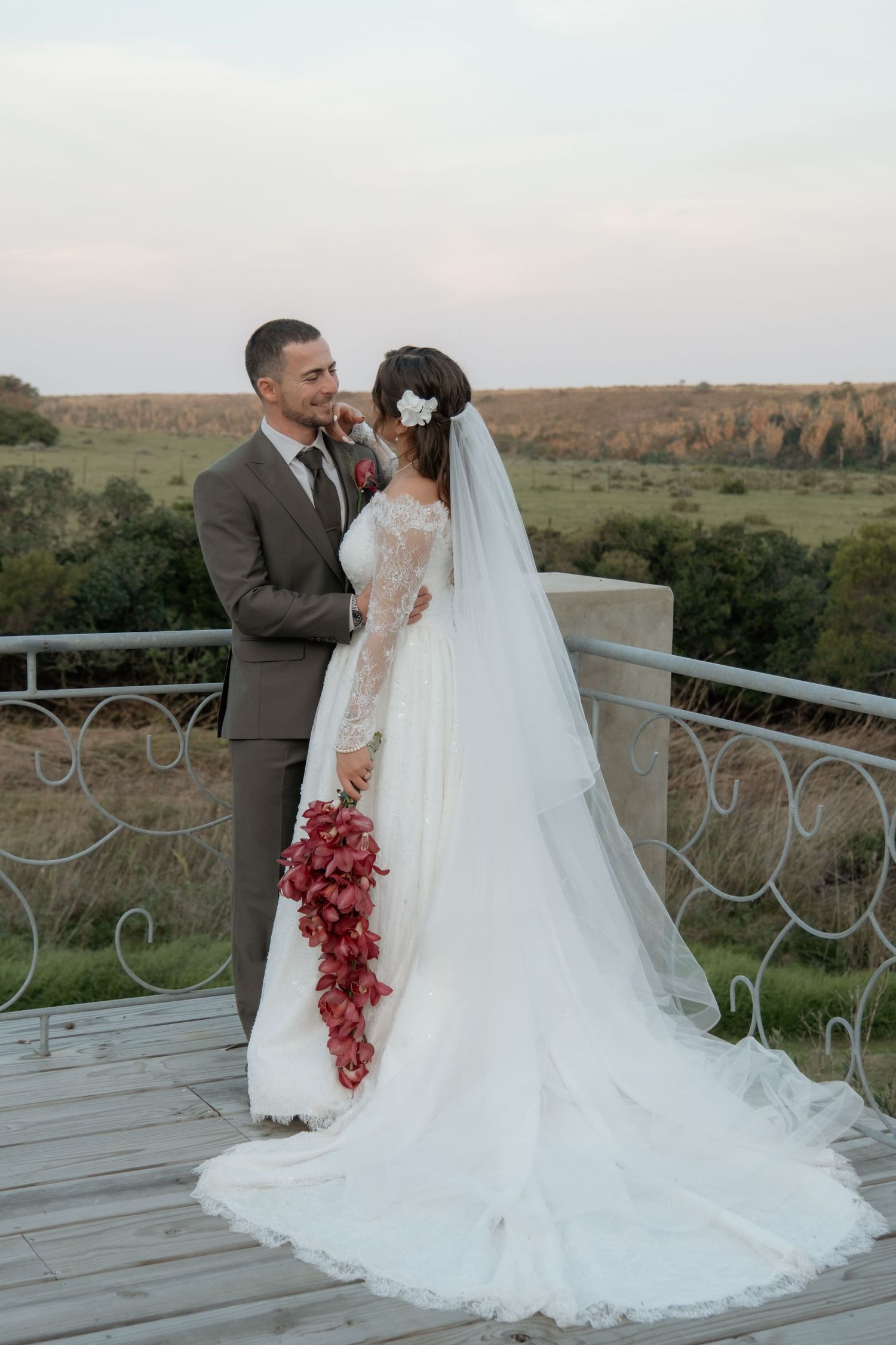 Bride and groom embracing on balcony overlooking scenic countryside at sunset wedding.