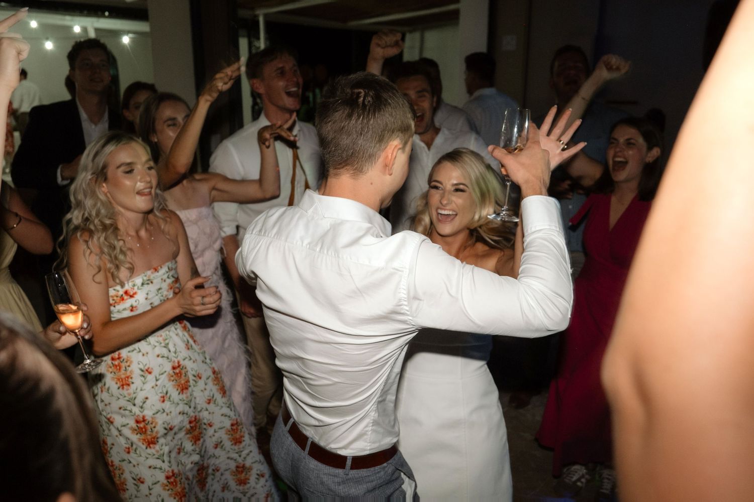Bride and groom dancing joyfully with excited wedding guests celebrating on the dance floor.