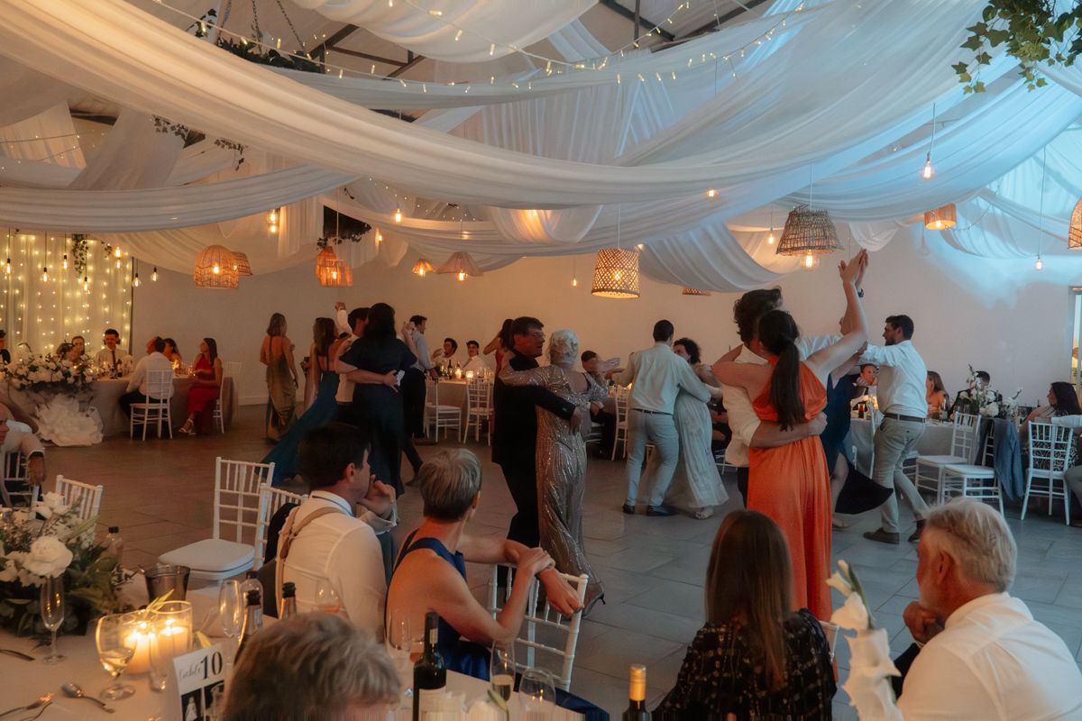 Guests dancing and celebrating on the dance floor at an elegant wedding reception with draped white ceiling.