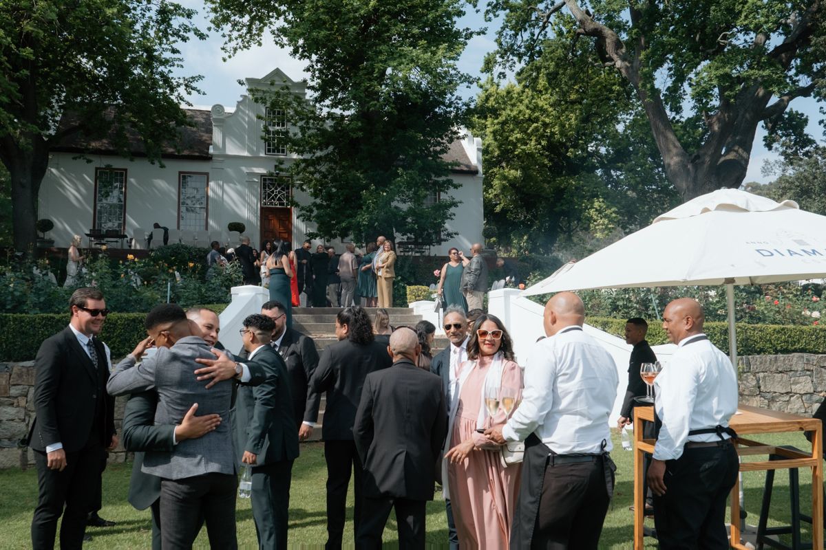 Wedding guests mingle and socialize in a lush outdoor garden setting following the ceremony.