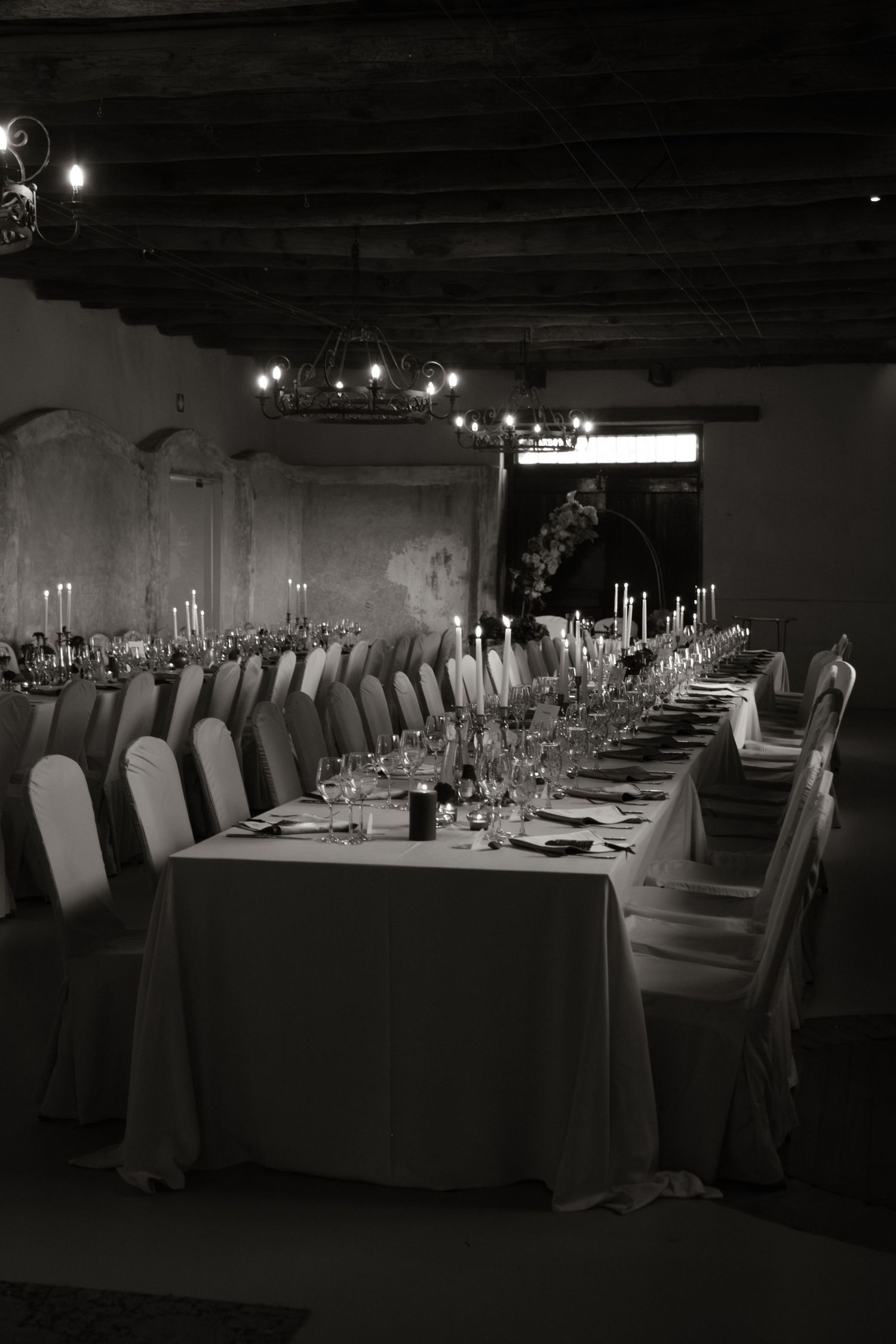 Black and white photo of elegantly set long wedding reception table with candles.