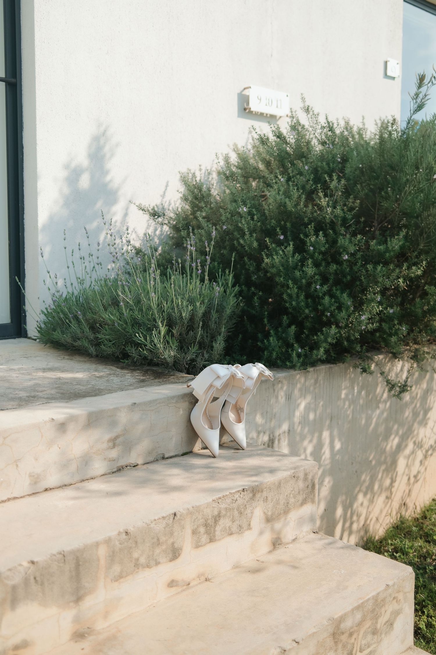 White bridal heels with ribbon on stone steps beside lush green garden shrubs.
