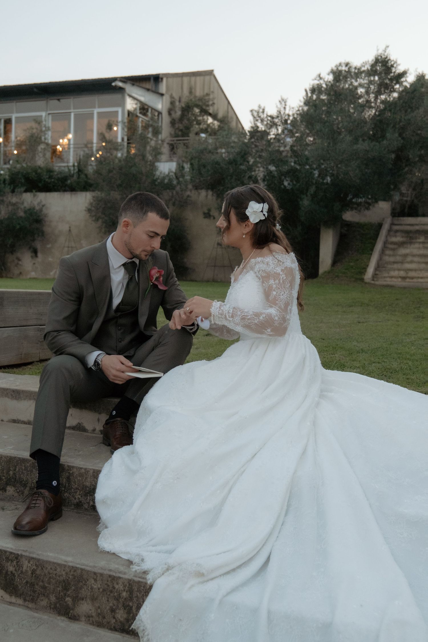 Bride and groom sit on stone steps reading wedding vows together at outdoor venue at dusk.