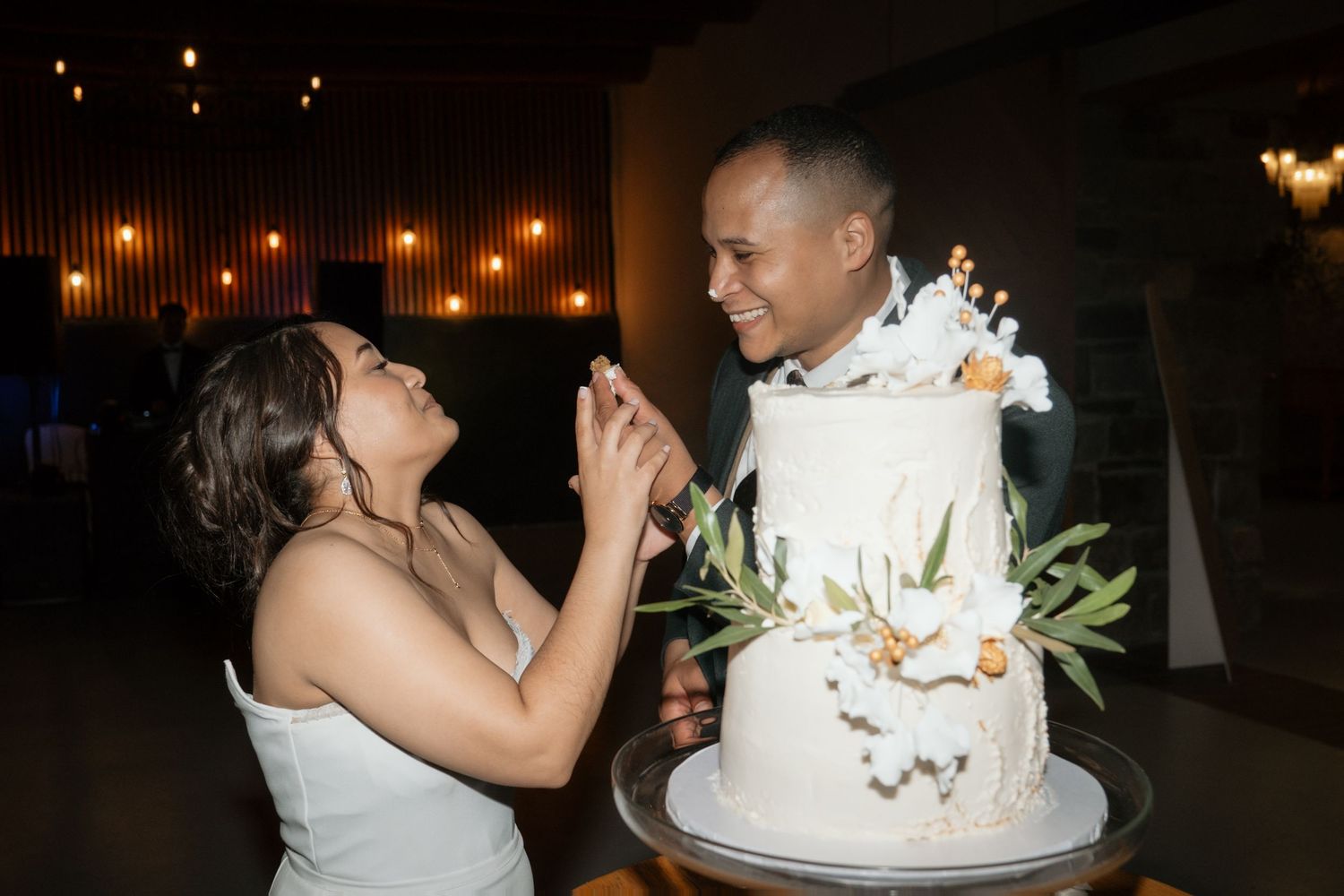 Bride and groom smiling while cutting their elegant white floral wedding cake.
