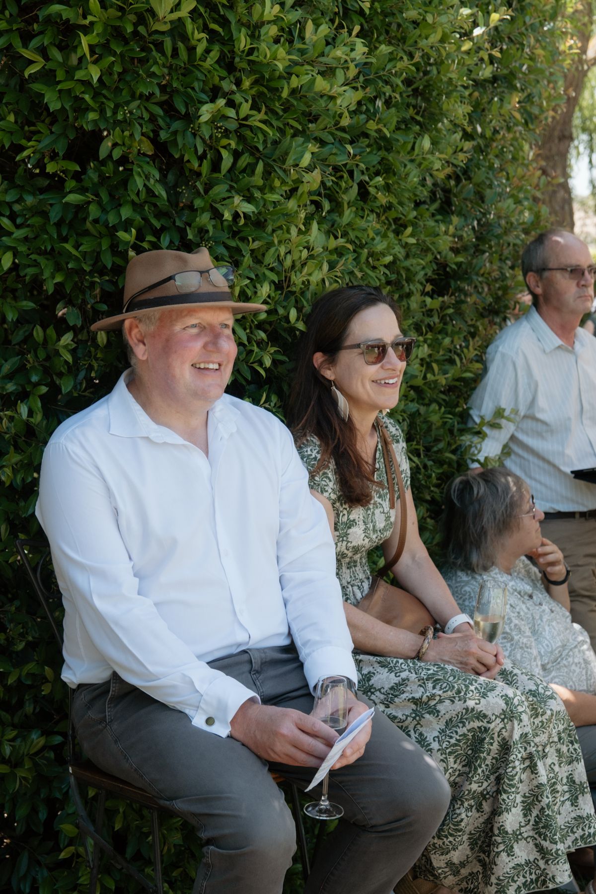 Smiling guests in summer attire seated outdoors at a garden wedding celebration.