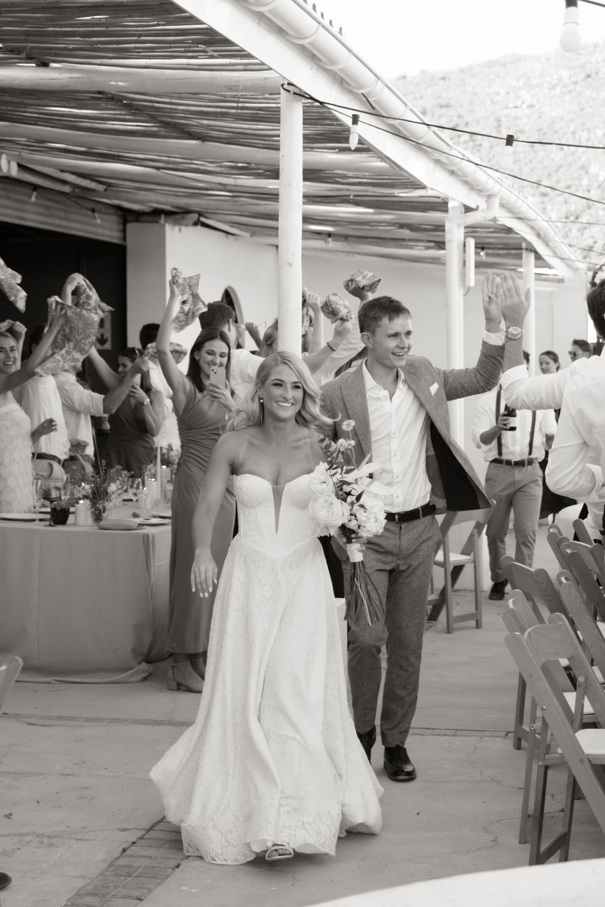 Black and white photo of bride and groom making grand entrance at outdoor wedding reception.