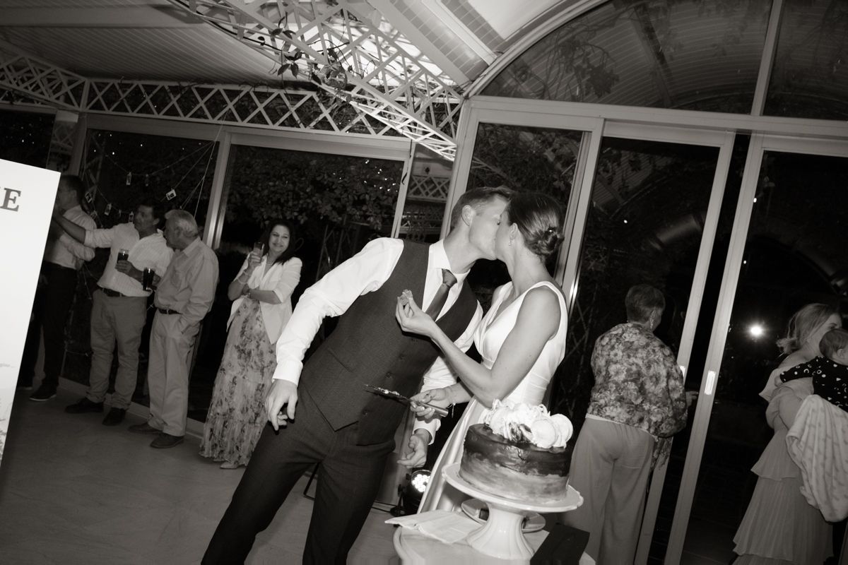 Black and white photo of bride and groom kissing beside wedding cake on dance floor at reception.