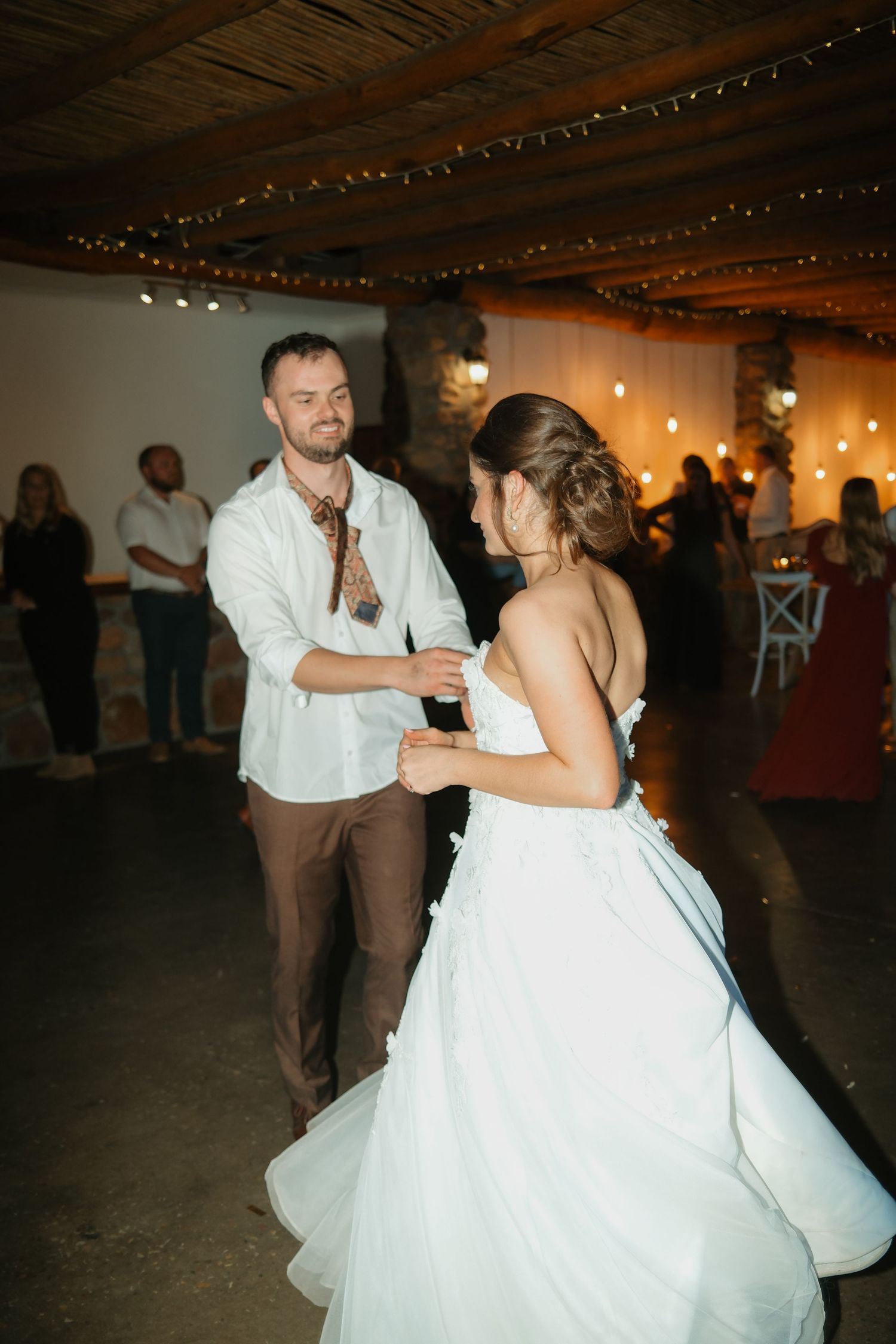 Groom in white shirt and brown pants shares first dance with bride at romantic reception.