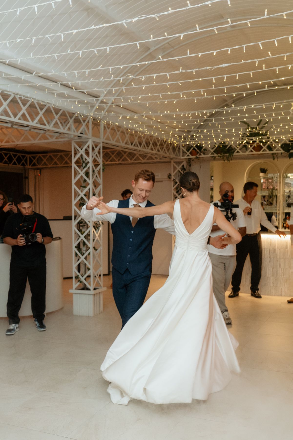 A bride and groom share their first dance under twinkling fairy lights at an elegant wedding reception.
