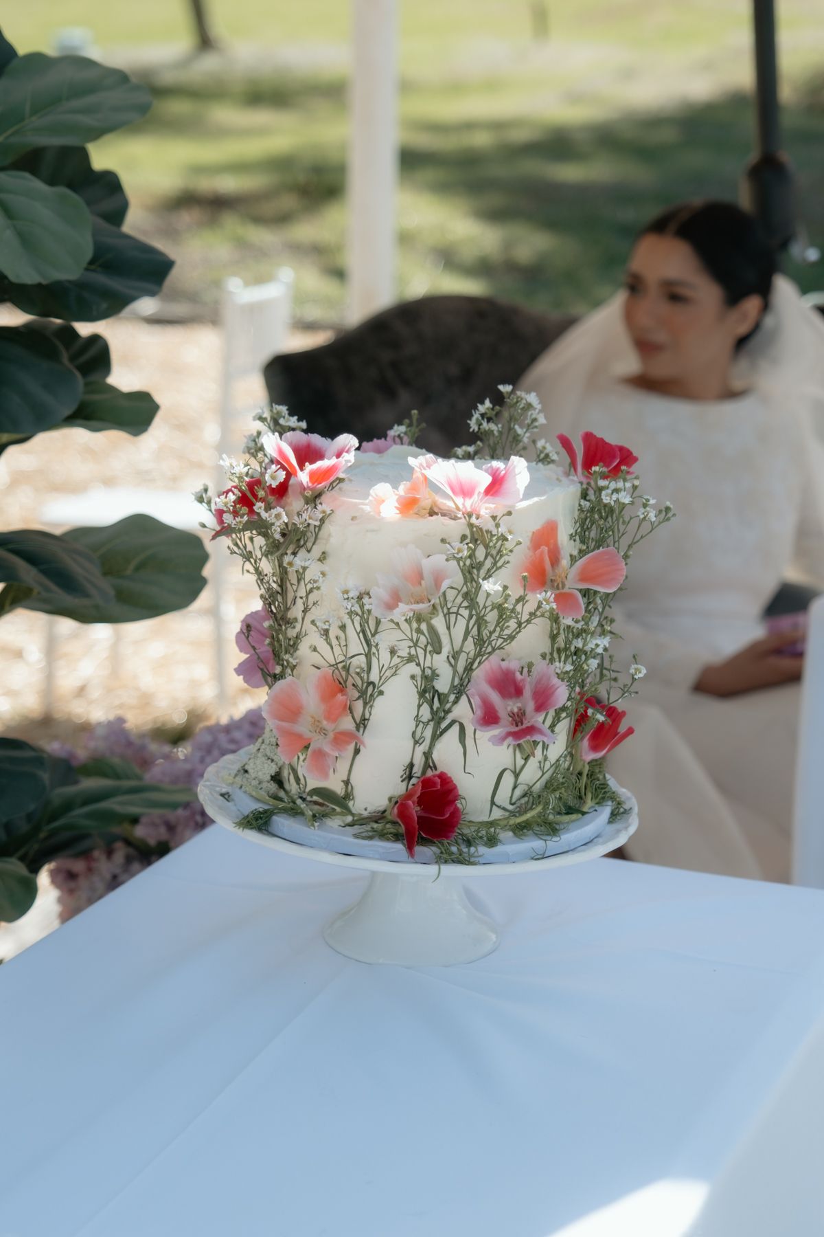 Elegant one-tier white wedding cake adorned with fresh pink and red flowers on a pedestal stand.