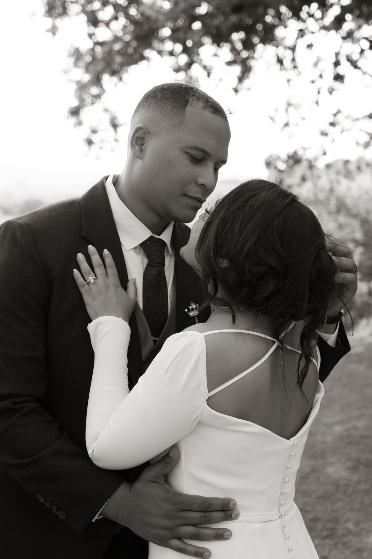 Black and white photo of bride and groom sharing an intimate embrace under a tree at their wedding.