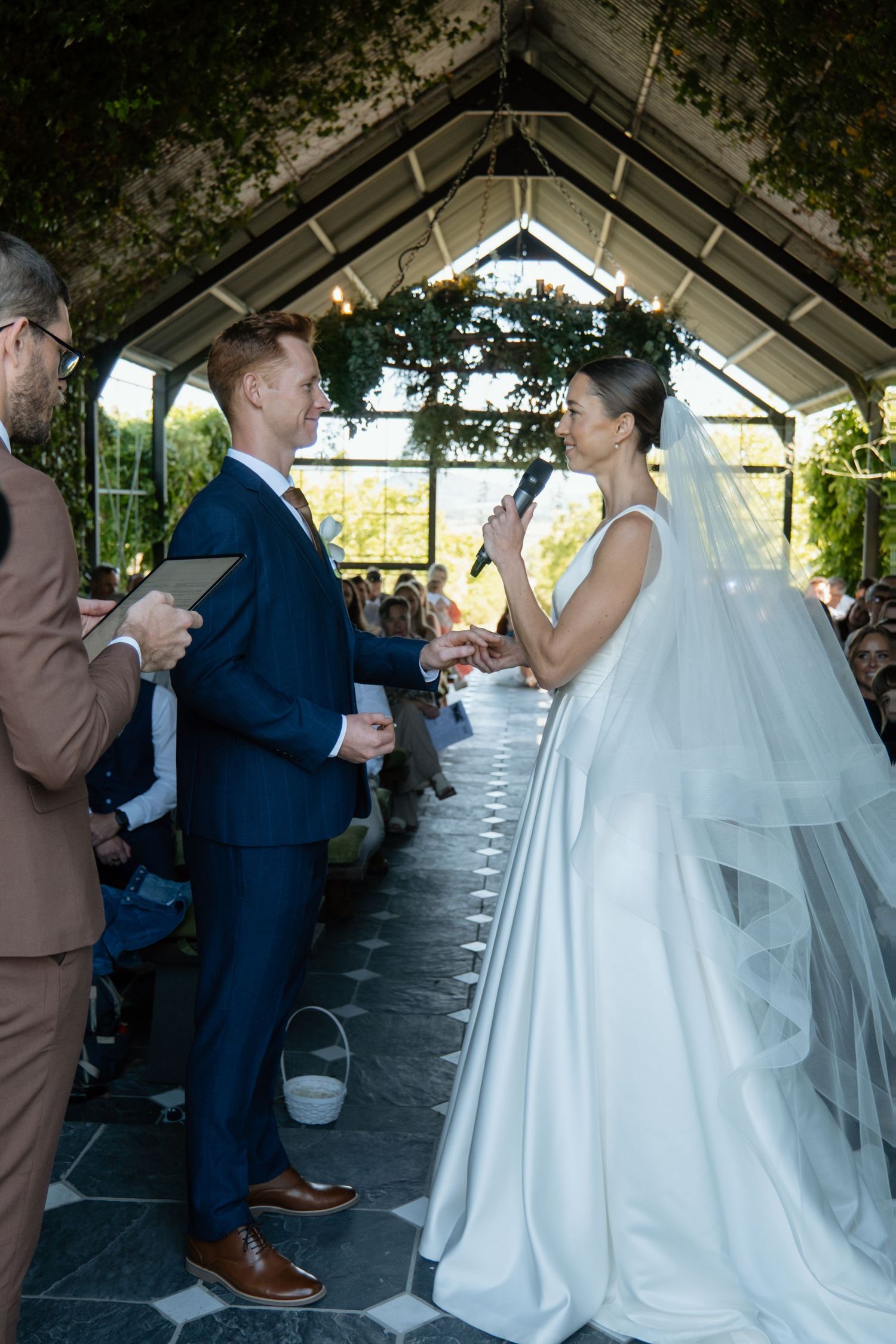 Bride reads vows to groom at outdoor wedding ceremony under floral arch.