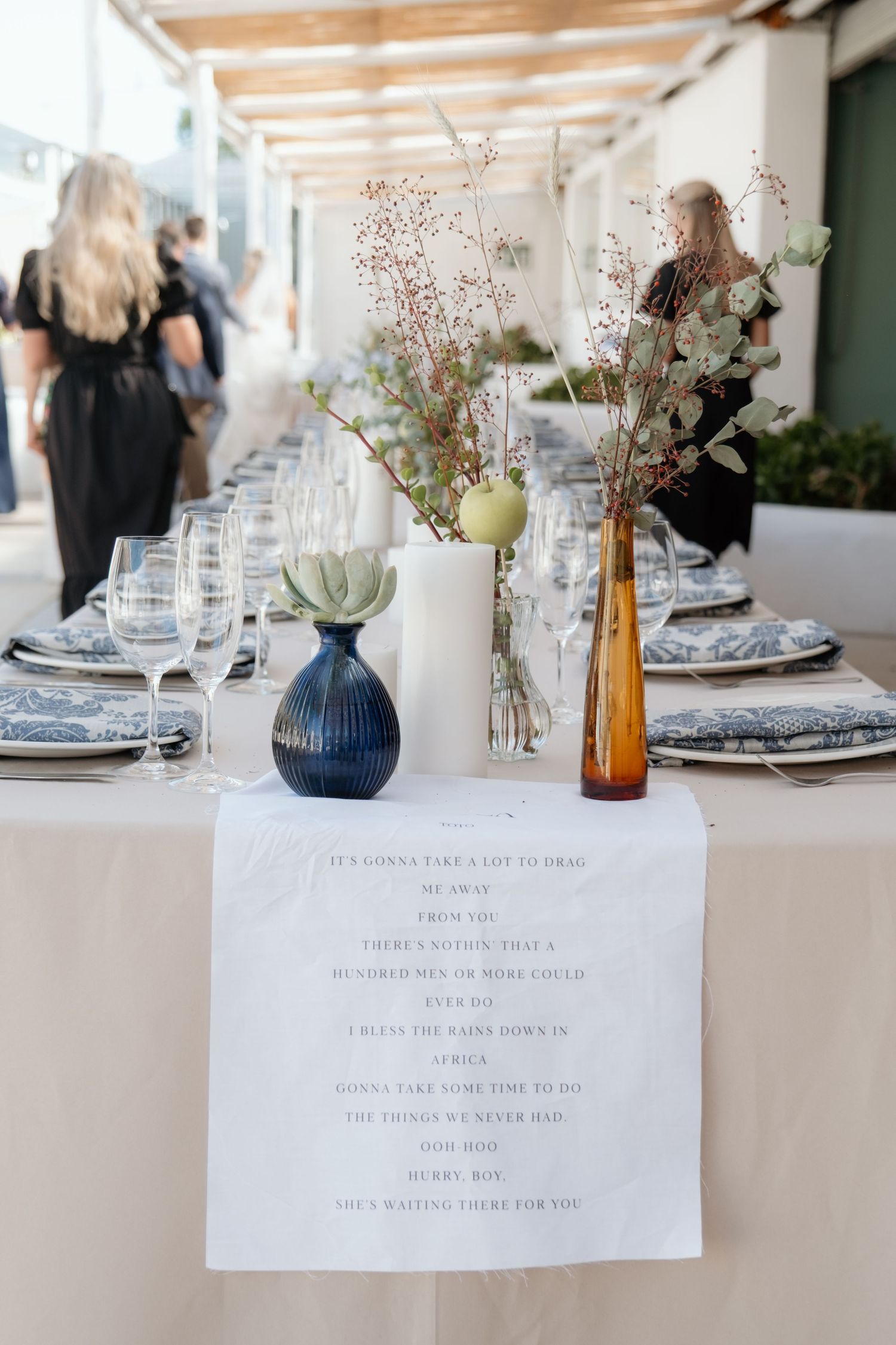 Elegant wedding reception table set with blue floral plates, bud vases, and lyric table runner.