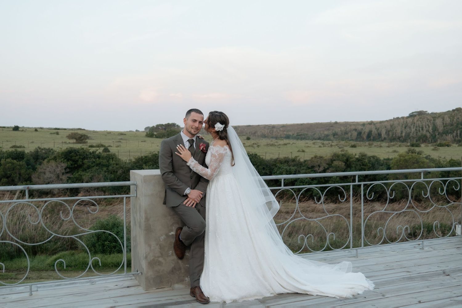Bride and groom pose elegantly on a stone terrace with sweeping countryside views during their golden hour wedding photos.