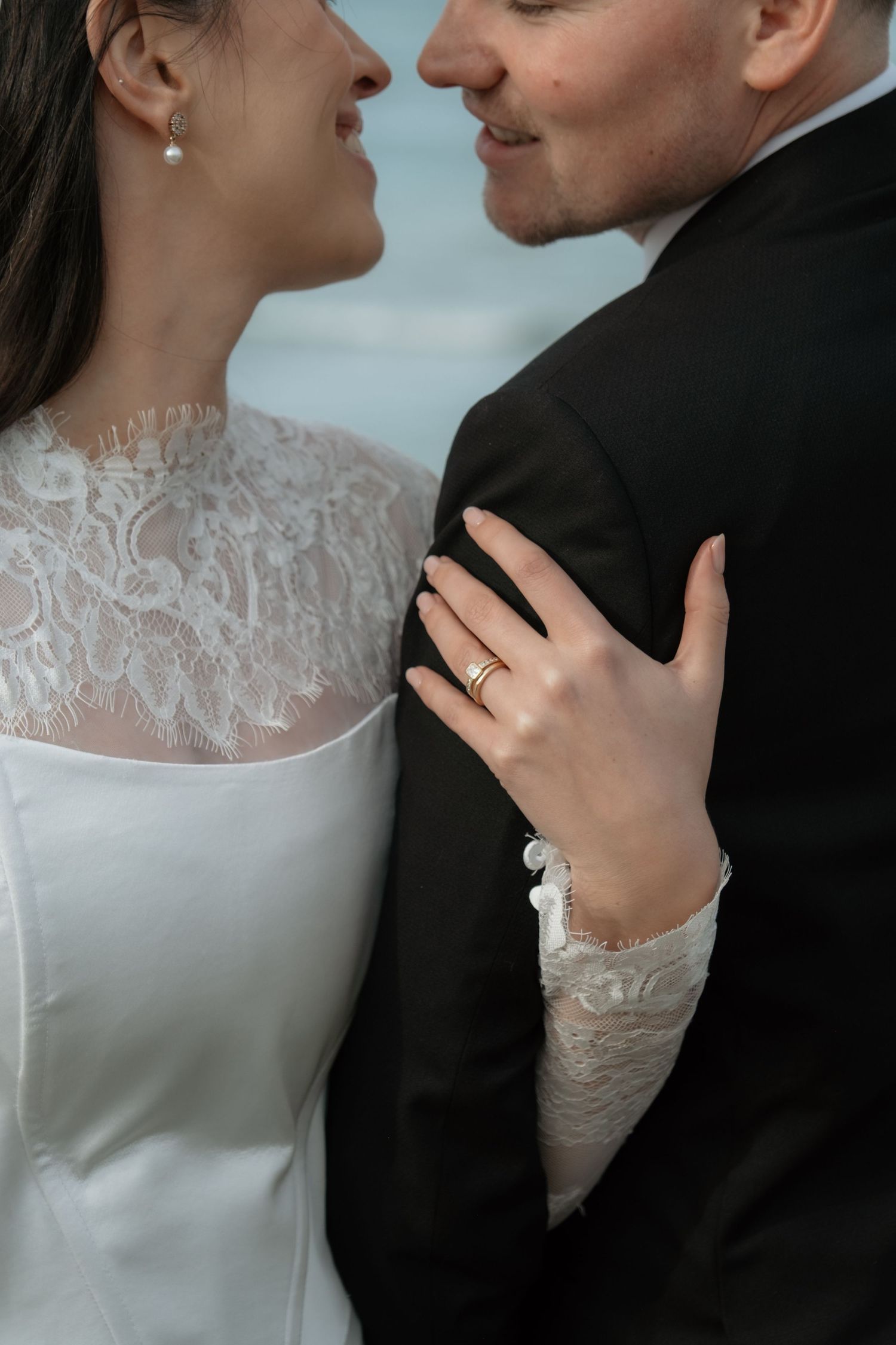 Close-up of bride and groom almost kissing, bride wearing lace wedding dress and gold wedding ring.