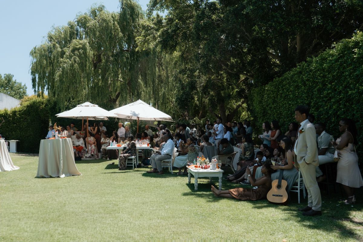 Elegant outdoor wedding reception on green lawn with white umbrellas, guests dining under weeping willow trees.