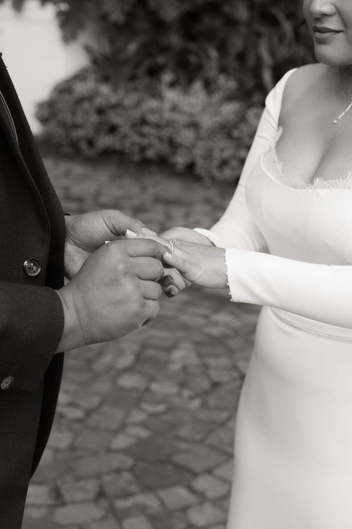 Black and white close-up of bride and groom exchanging rings during wedding ceremony.
