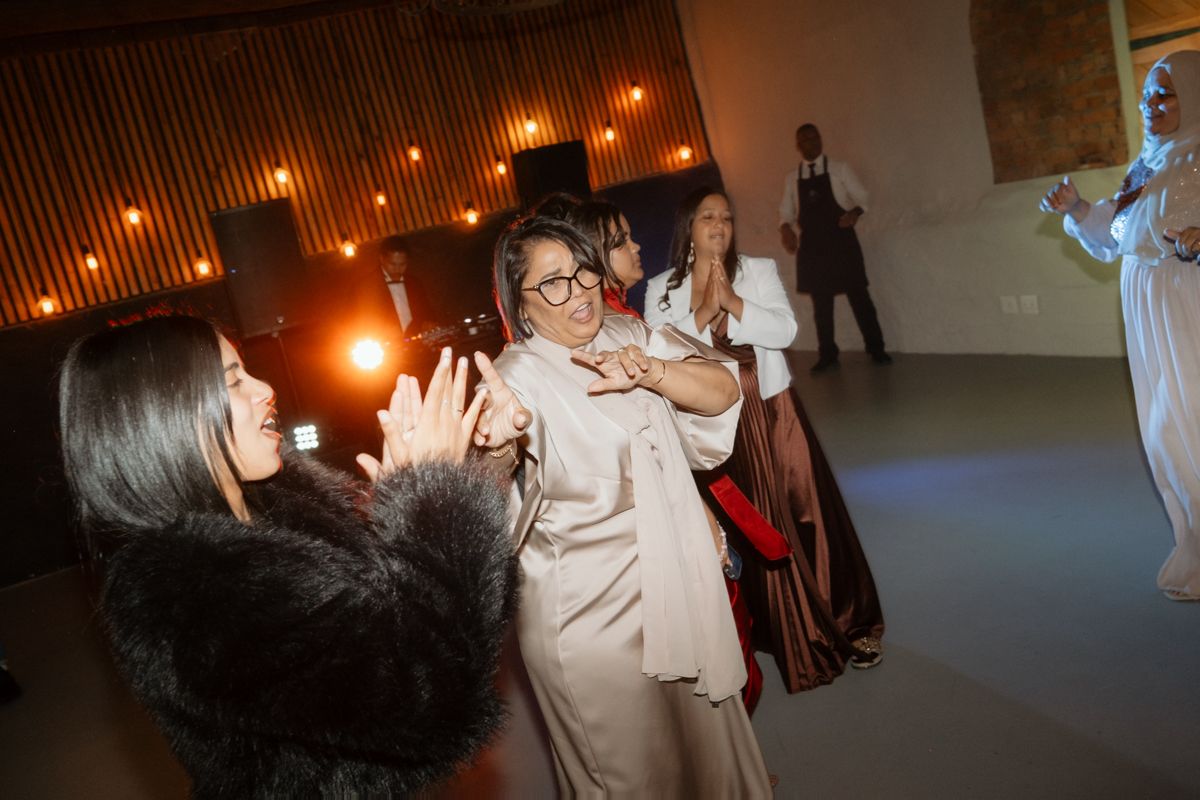 Wedding guests dance and celebrate joyfully on the dance floor at an indoor evening reception.