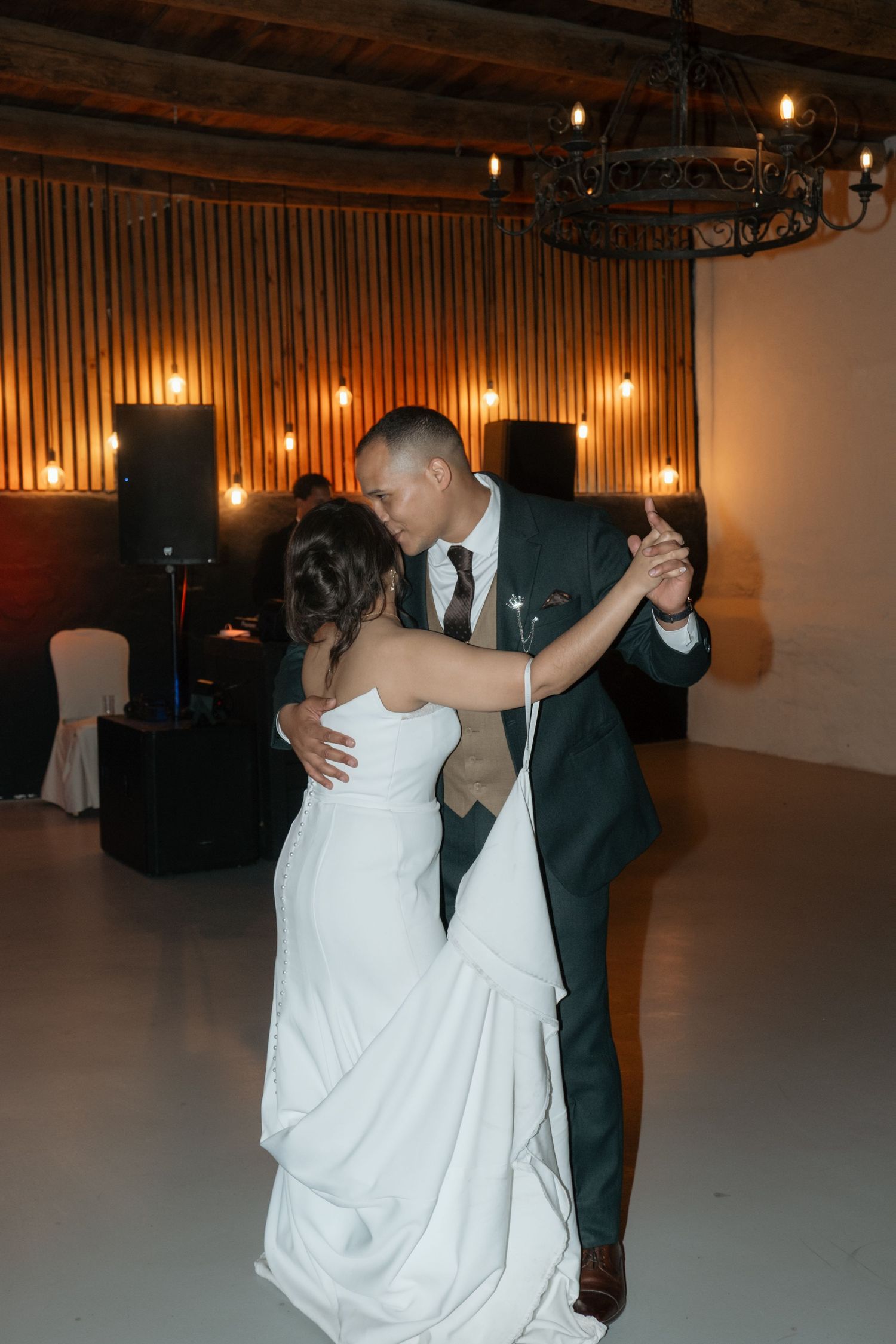 Bride and groom share romantic first dance in warmly lit wedding reception venue.