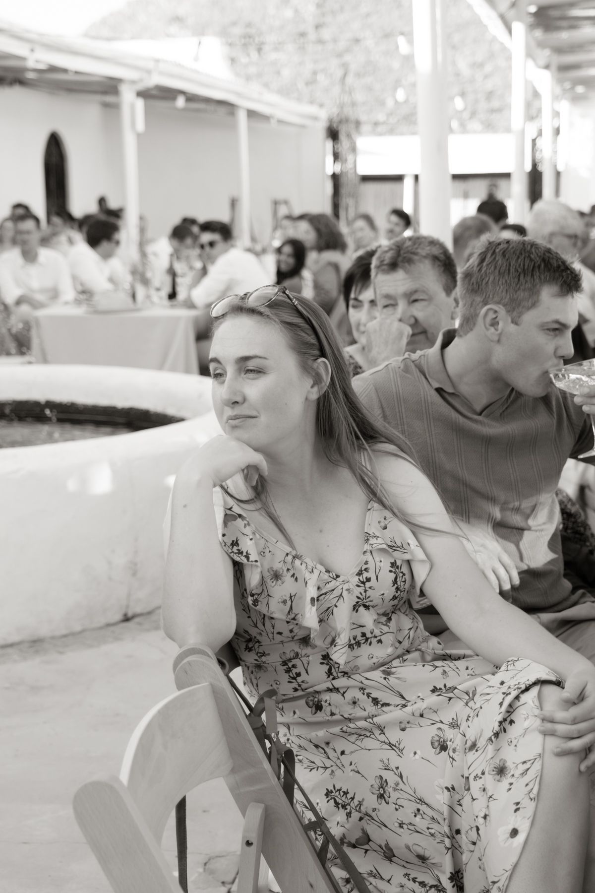 Black and white photo of a young woman in a floral dress listening attentively at a wedding reception.