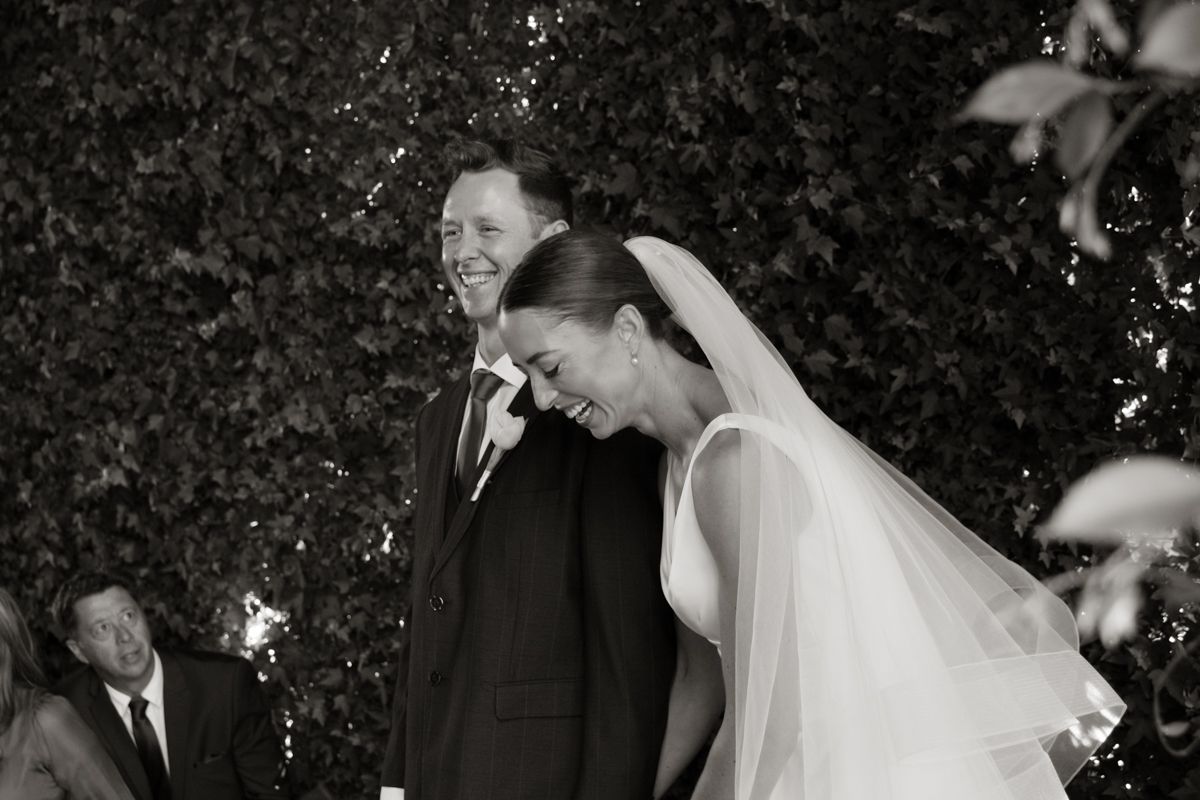 Black and white photo of laughing bride and groom sharing a joyful moment at their wedding ceremony.