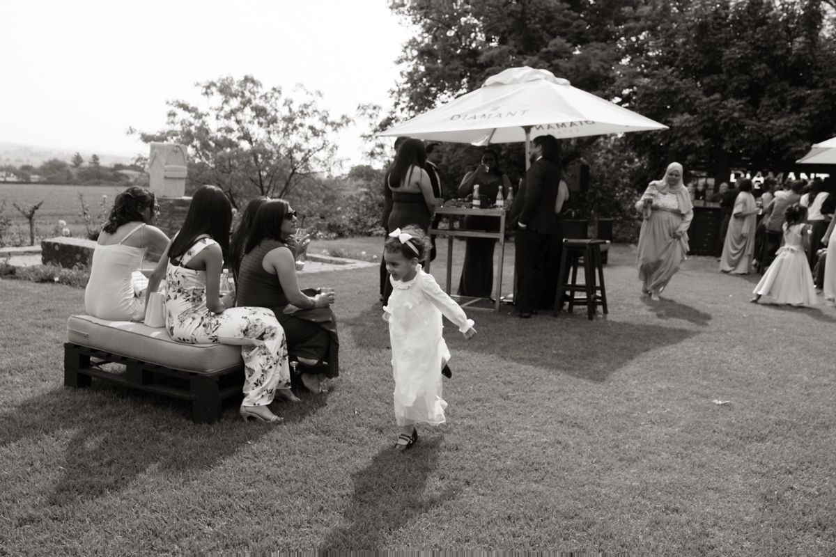 Black and white photo of child running across lawn at outdoor wedding reception with guests seated nearby.