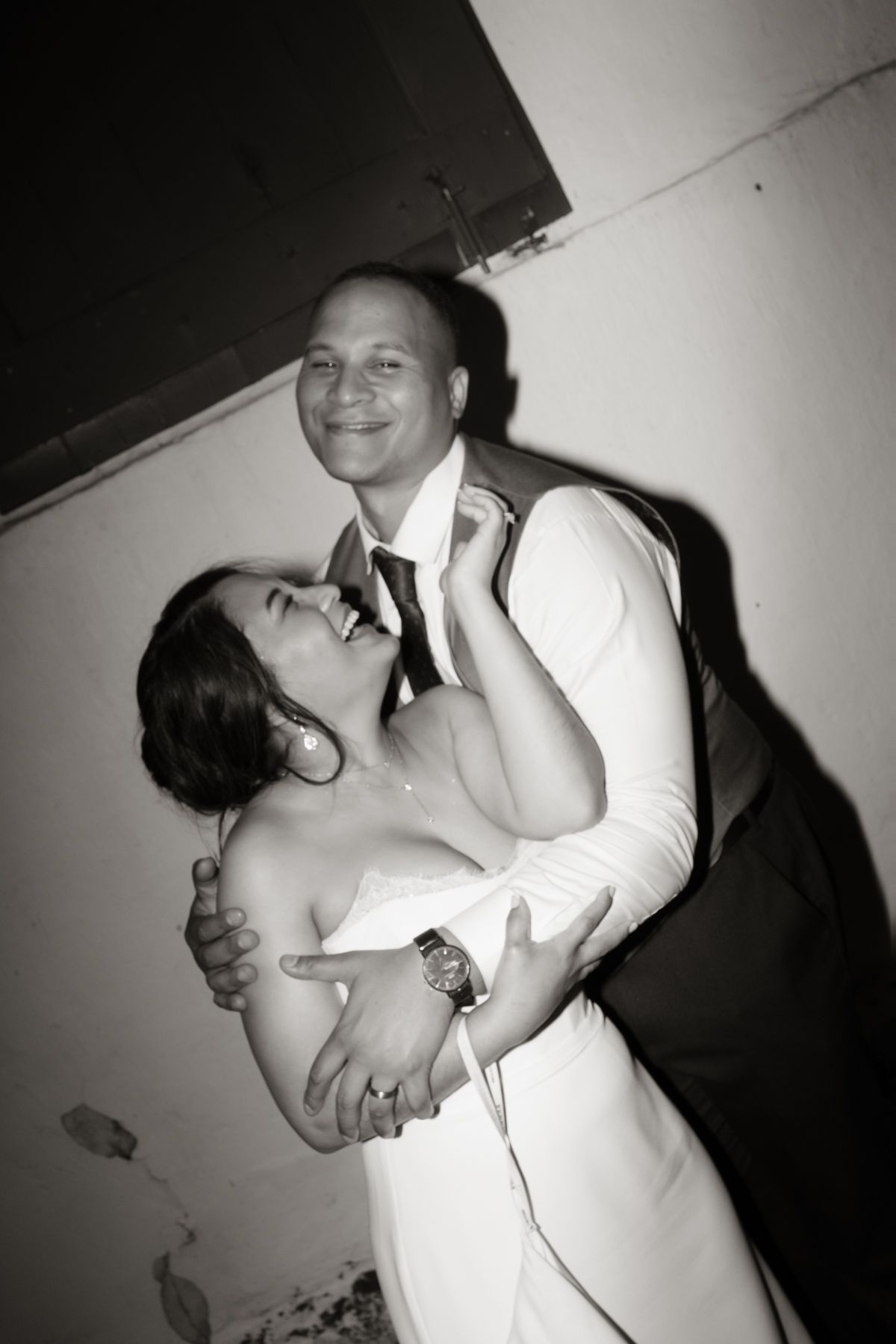 Black and white photo of laughing bride and smiling groom sharing a joyful embrace on the dance floor.