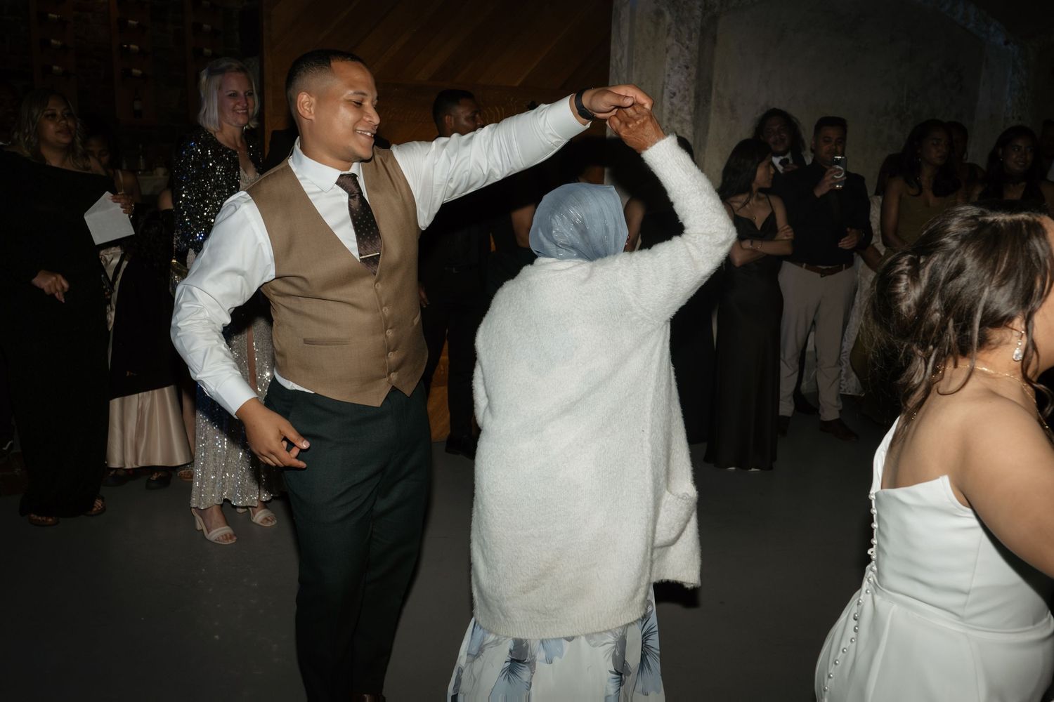 Groom in vest and tie dancing joyfully with an elderly guest on the wedding reception dance floor.