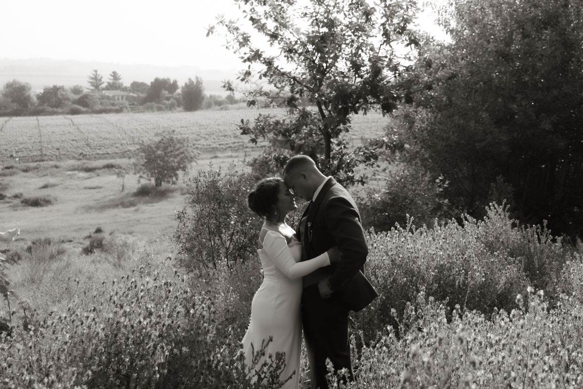 Bride and groom share an intimate moment among wildflowers in romantic black and white wedding photo.