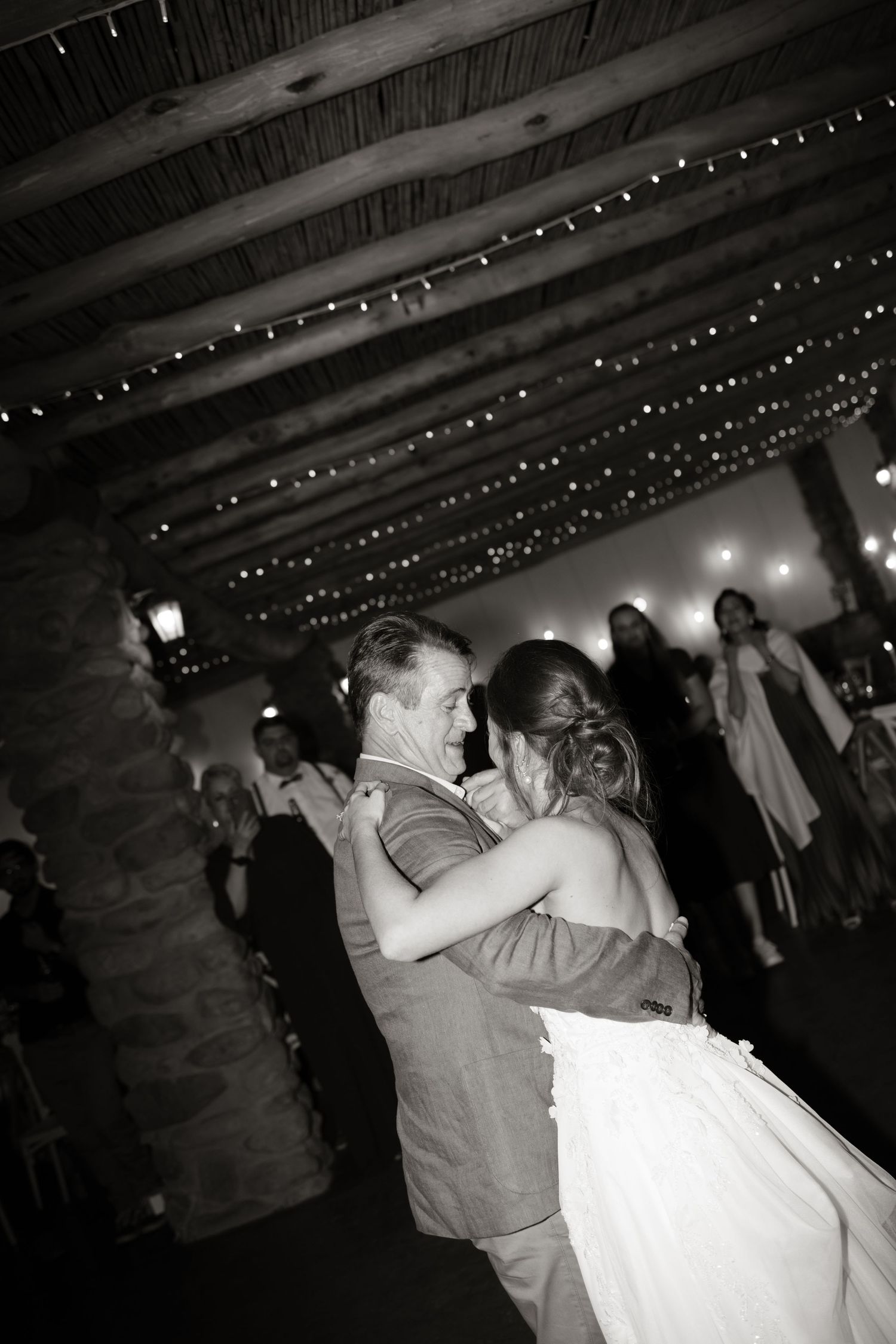 Bride and groom share their first dance under twinkling fairy lights at a rustic wedding reception.