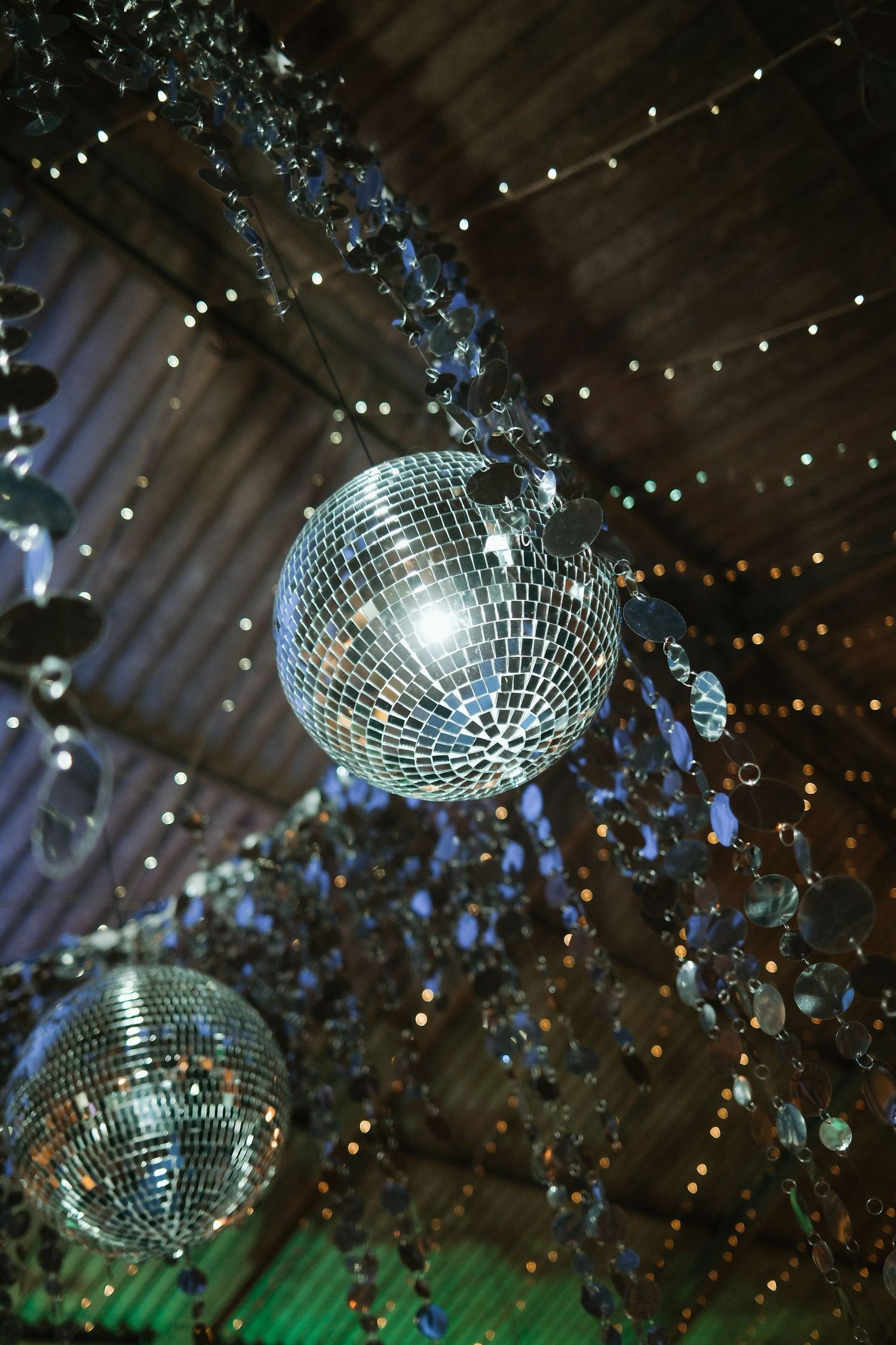 Shimmering disco mirror balls hanging from a decorated ceiling with crystal garlands and twinkling fairy lights.