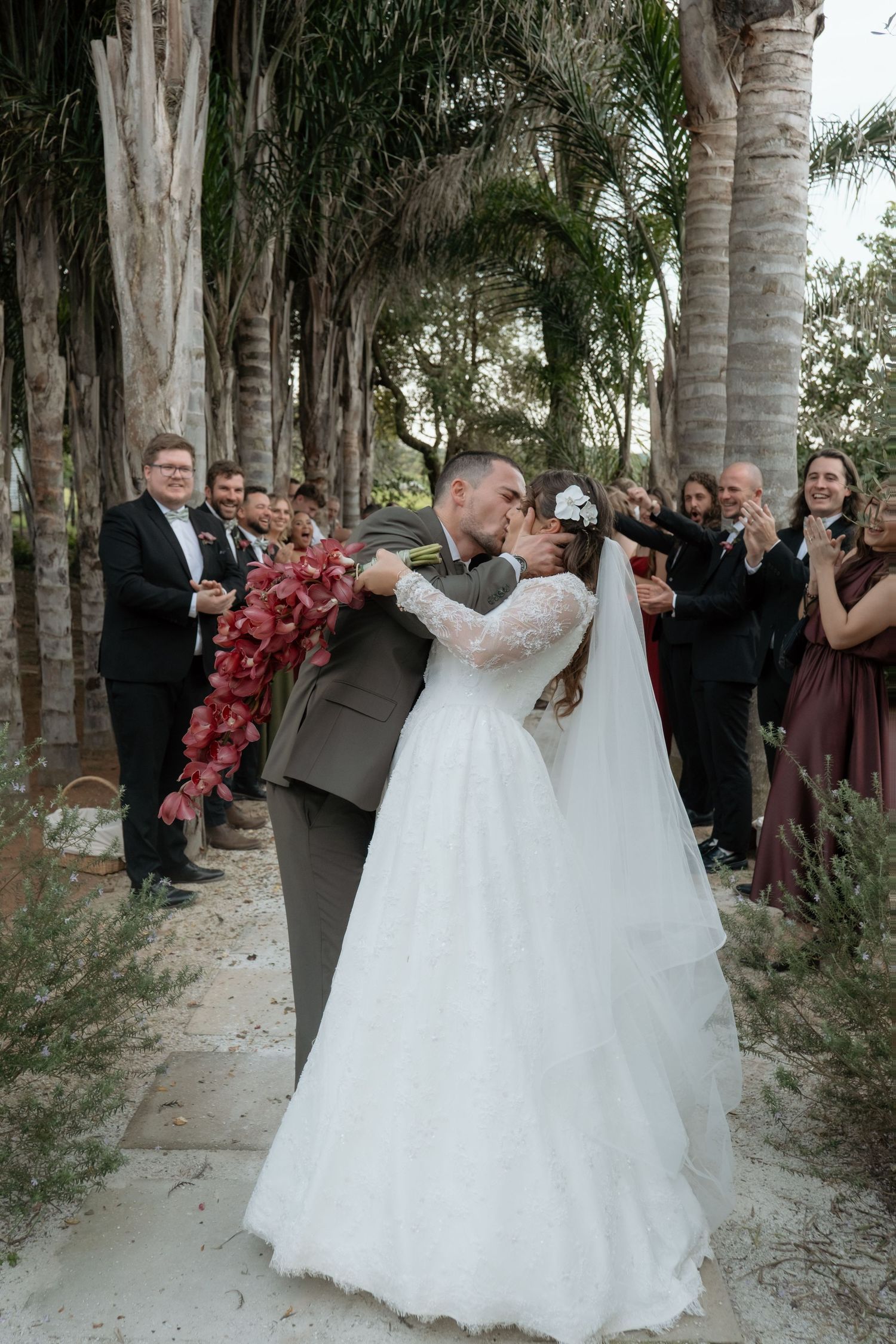 Bride and groom share first kiss as newlyweds while guests celebrate along outdoor wedding aisle.