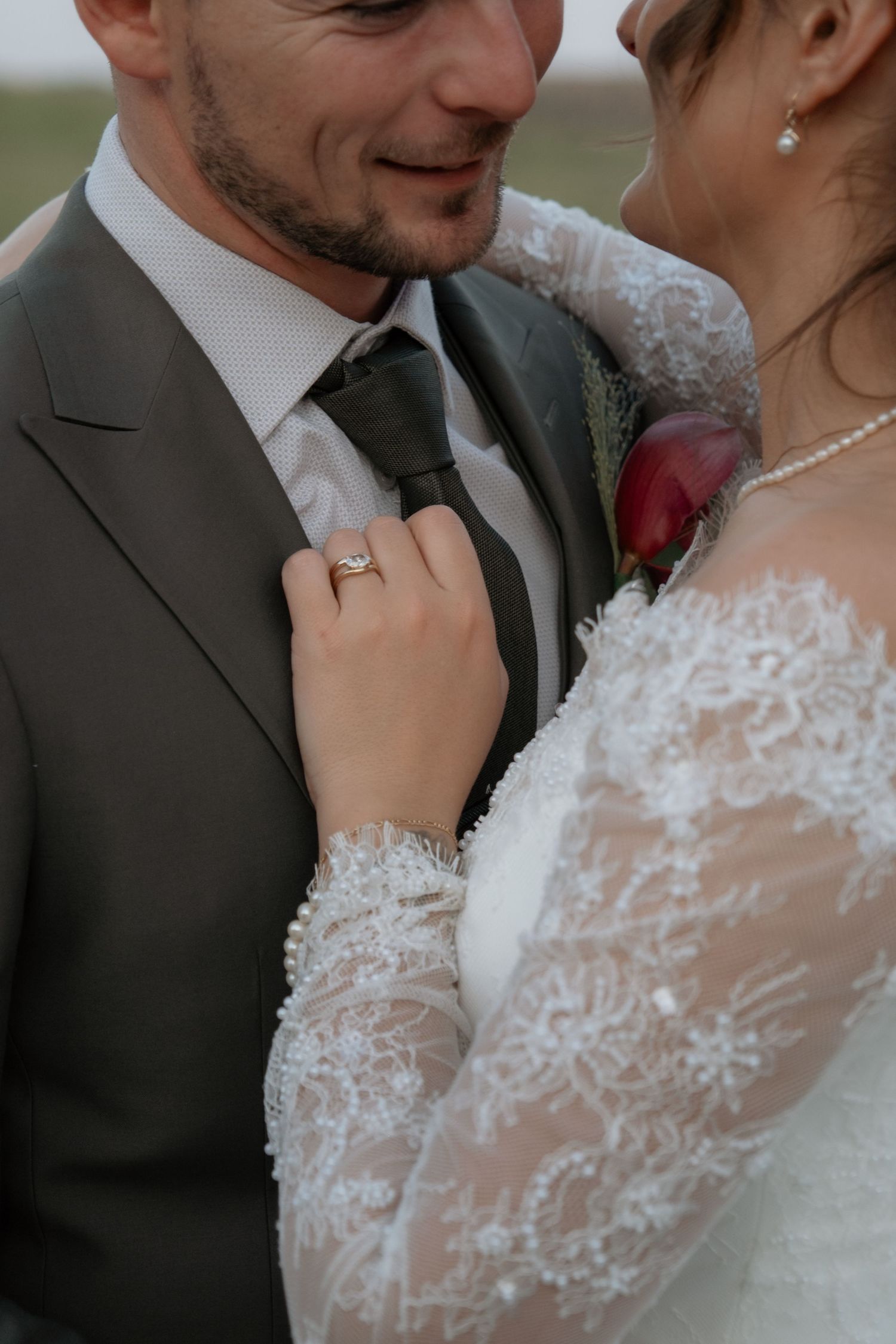 Bride in lace gown adjusting grooms tie showing diamond engagement ring close-up.