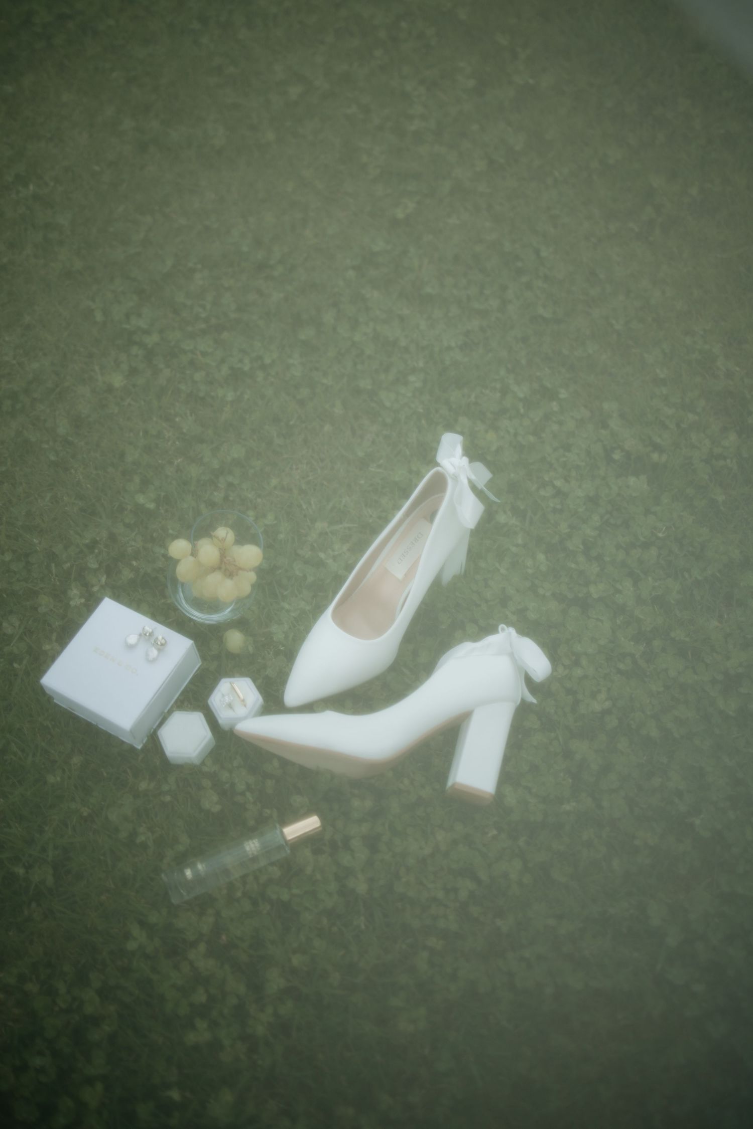Wedding accessories including white heels and small details arranged on green surface at Wildekrans Venue
